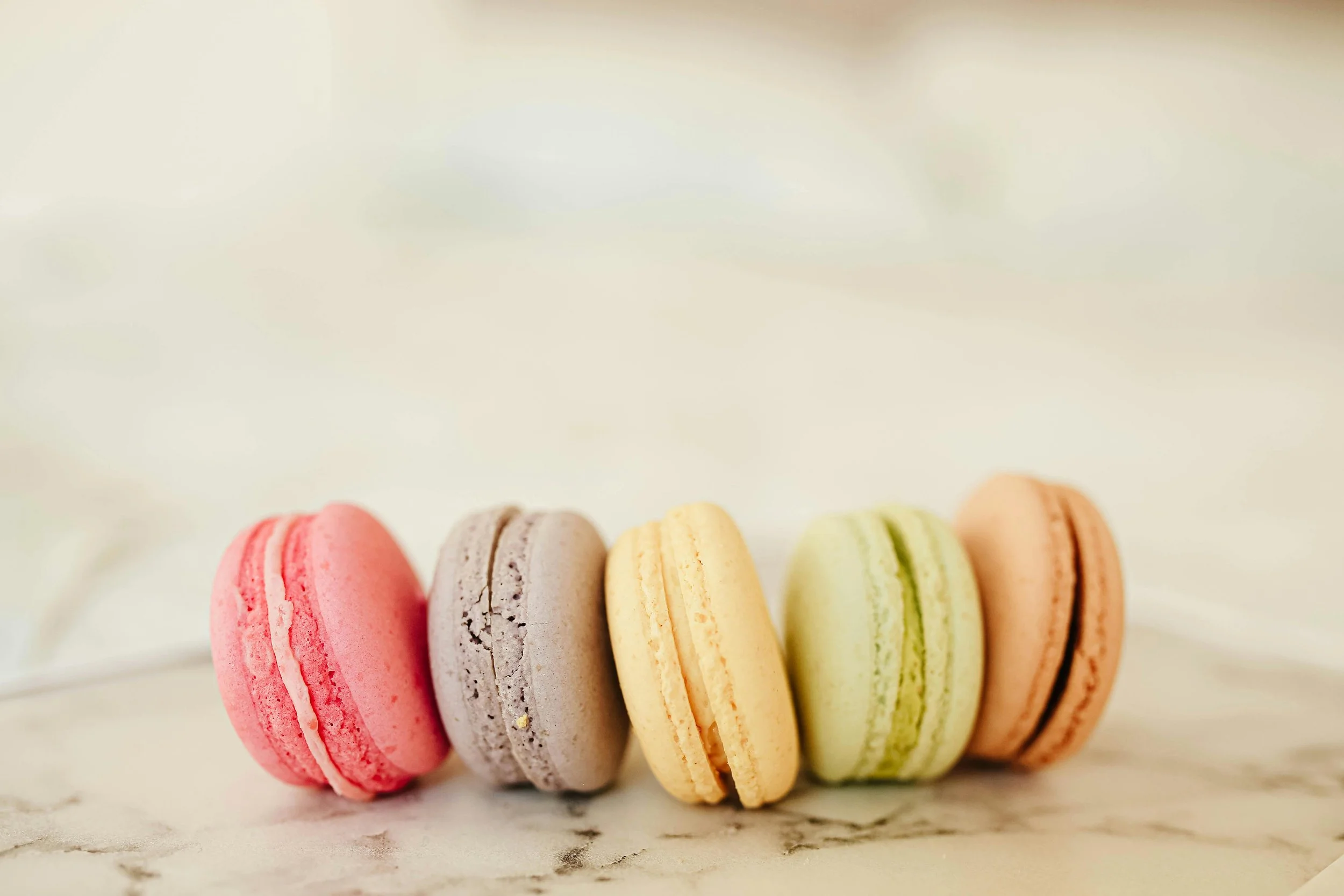 A line of different coloured French macarons on a marble surface