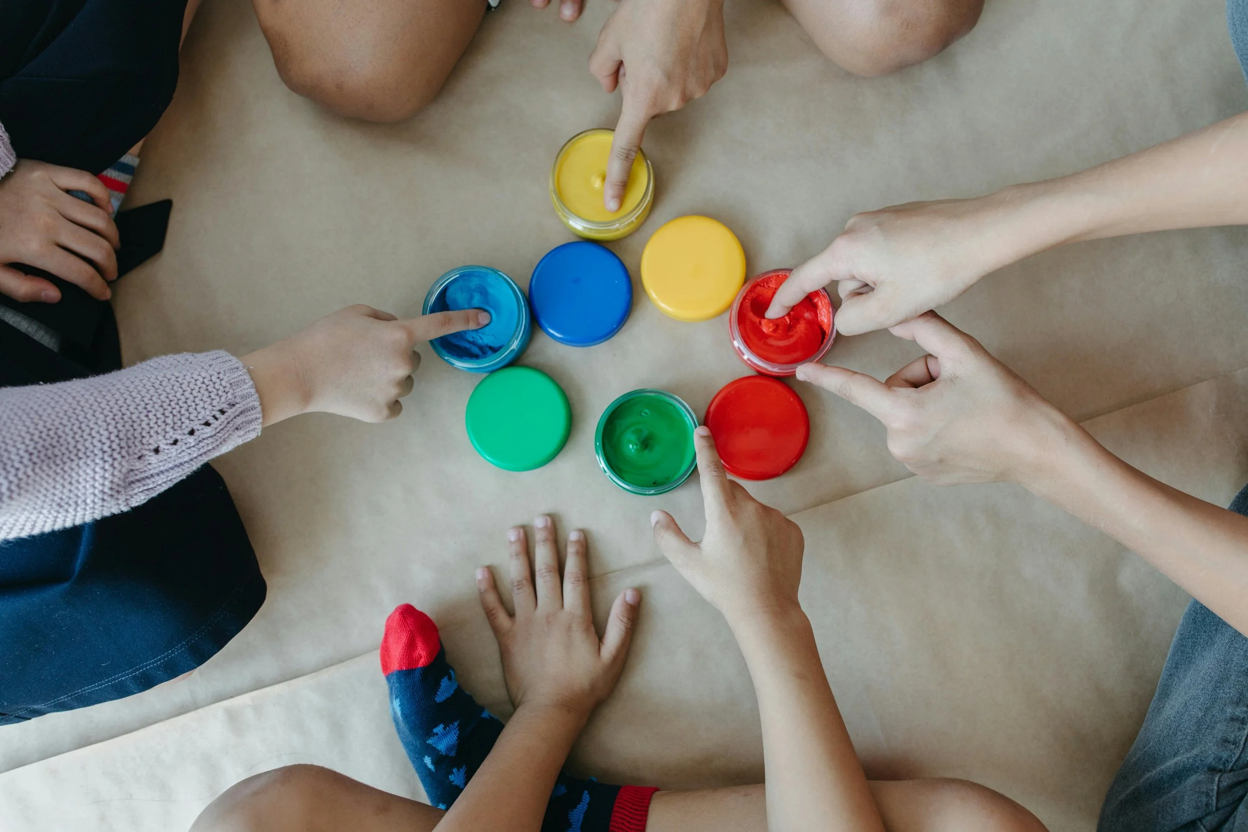 A group of children sitting in a circle learning French colours with different coloured paint including red, blue, yellow and green.