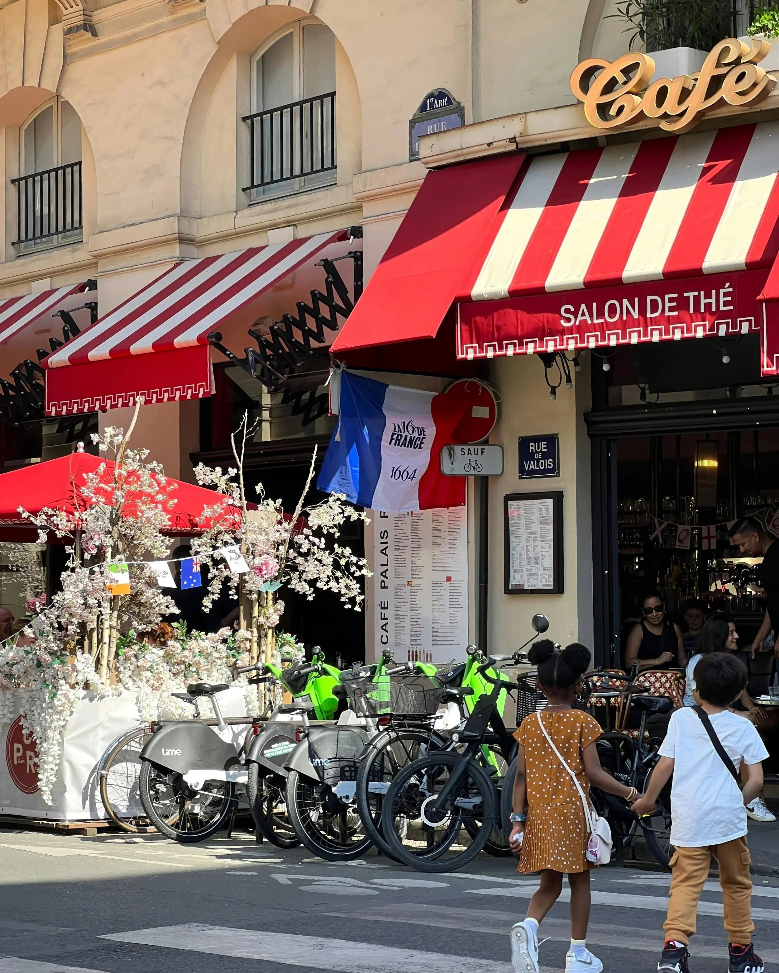 A typical French street with french flags, bicycles and young children holding hands while crossing the road.