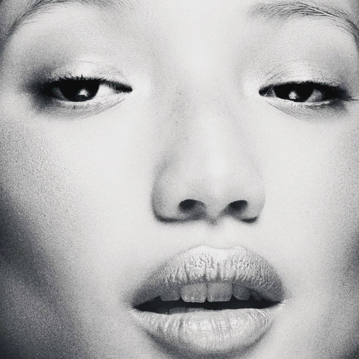 Close-up black and white photo of a person's face, focusing on their eyes, nose, and lips. The person's eyes are partially closed, and their lips are slightly parted.