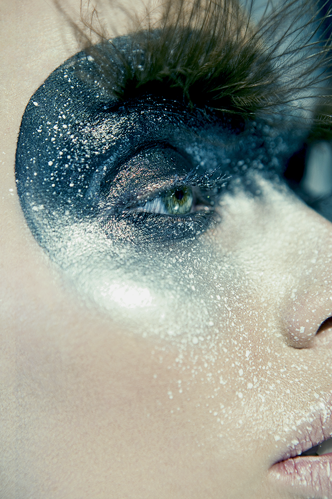 Close-up of a person's eye with artistic black and white face makeup and glitter.