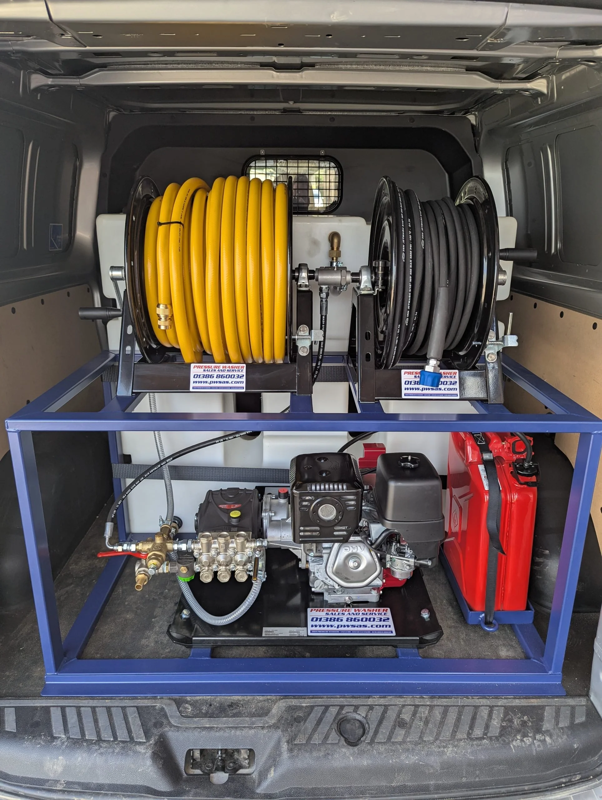 Equipment for vehicle pressure washing, including yellow and black hoses on reels, a high-pressure washer engine, and a red fuel container, all stored inside a vehicle's rear area.