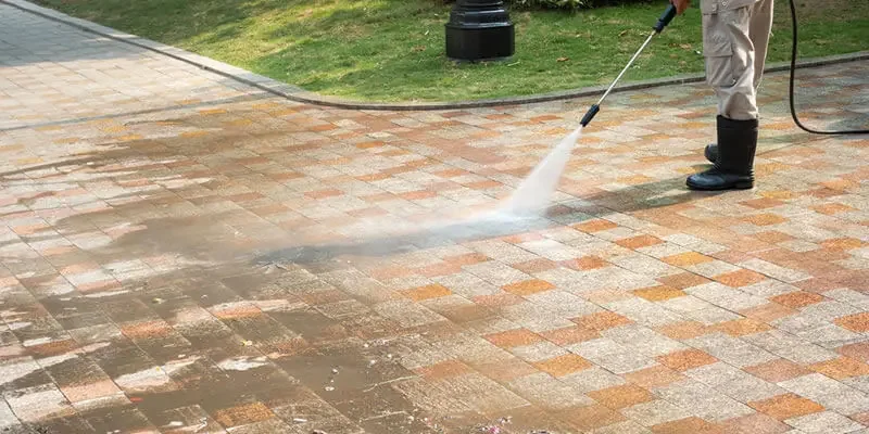 Person power washing a brick patio with a high-pressure hose.
