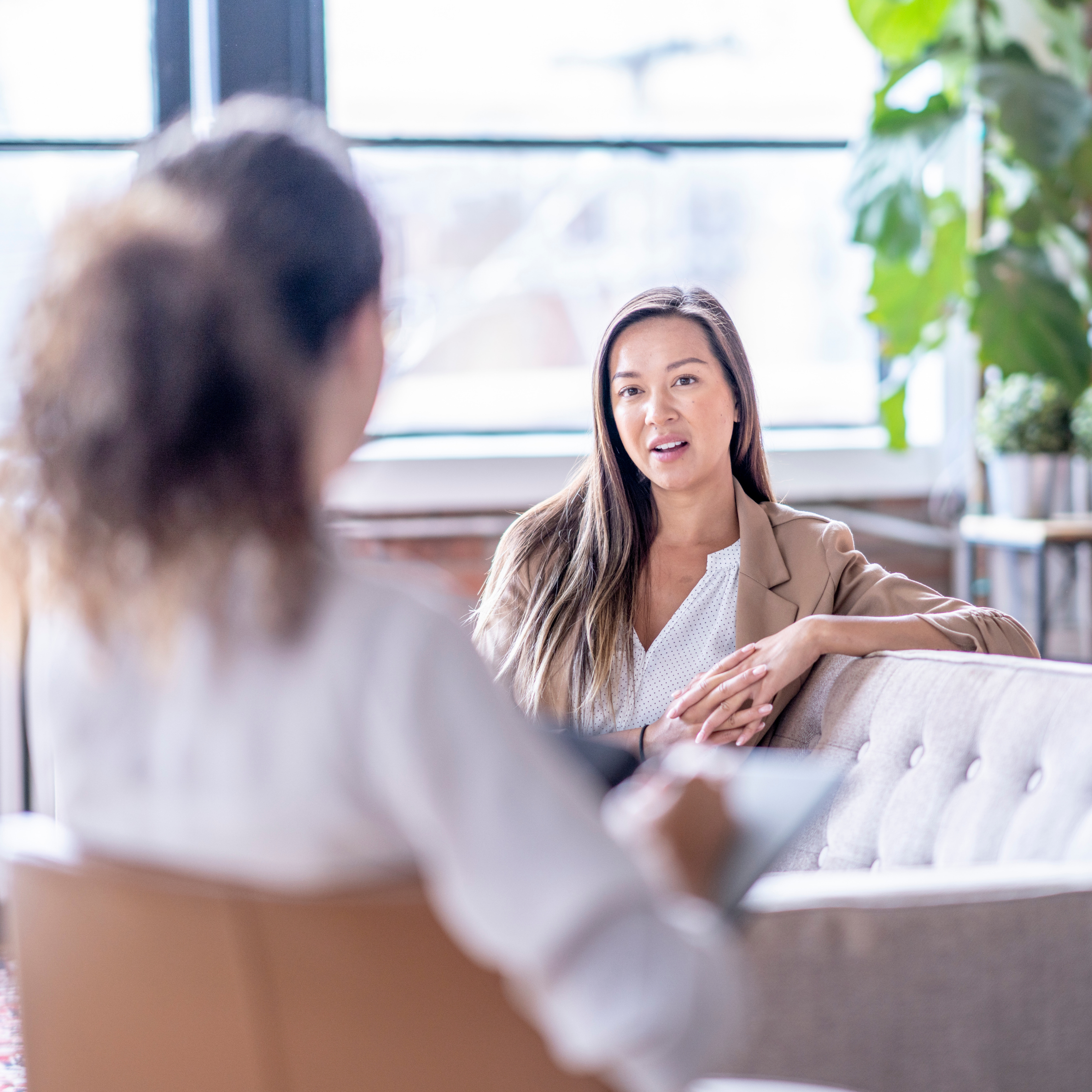 Two women having a conversation in a bright, modern cafe, one woman in focus and the other blurred in the foreground.