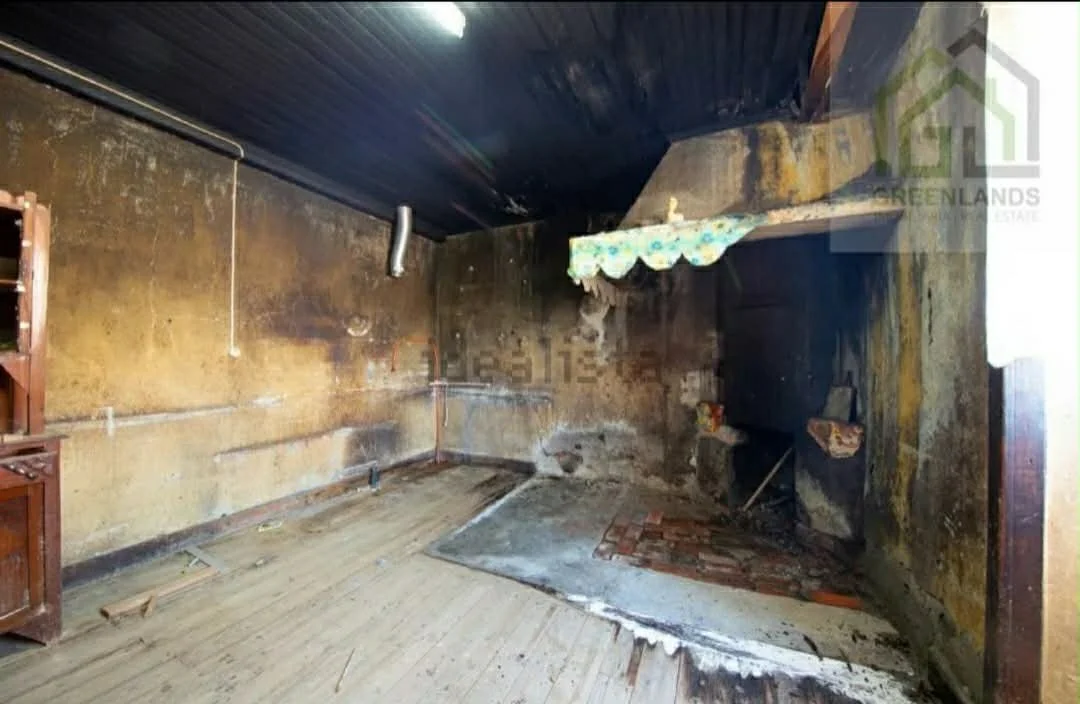Burnt and damaged interior of a room with soot-covered walls, a partially burned fireplace, and a charred ceiling.