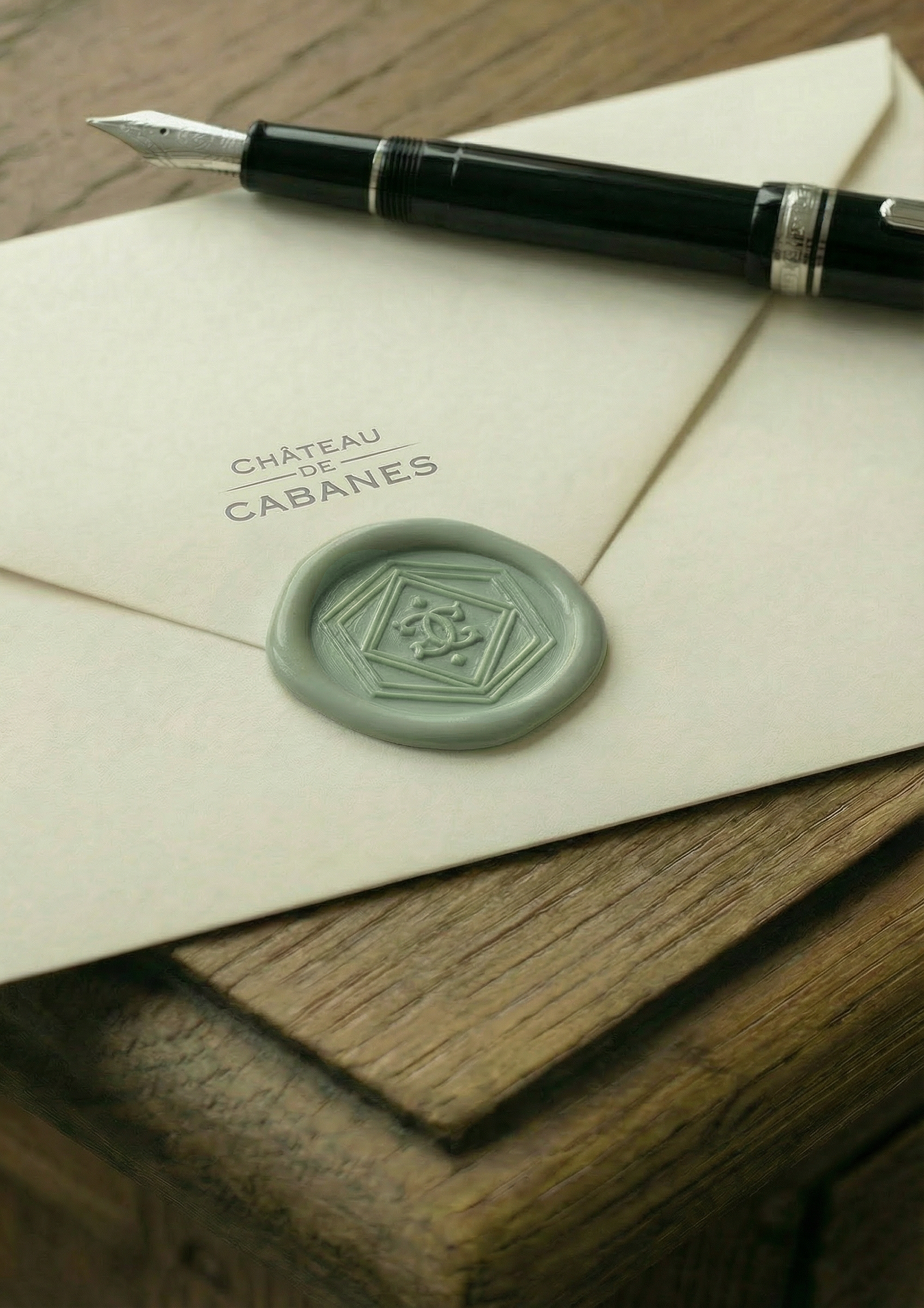 A letter with a wax seal, a fountain pen, and a closed notebook on a wooden surface. The letter has the text 'Château de Cabanes' printed on it.