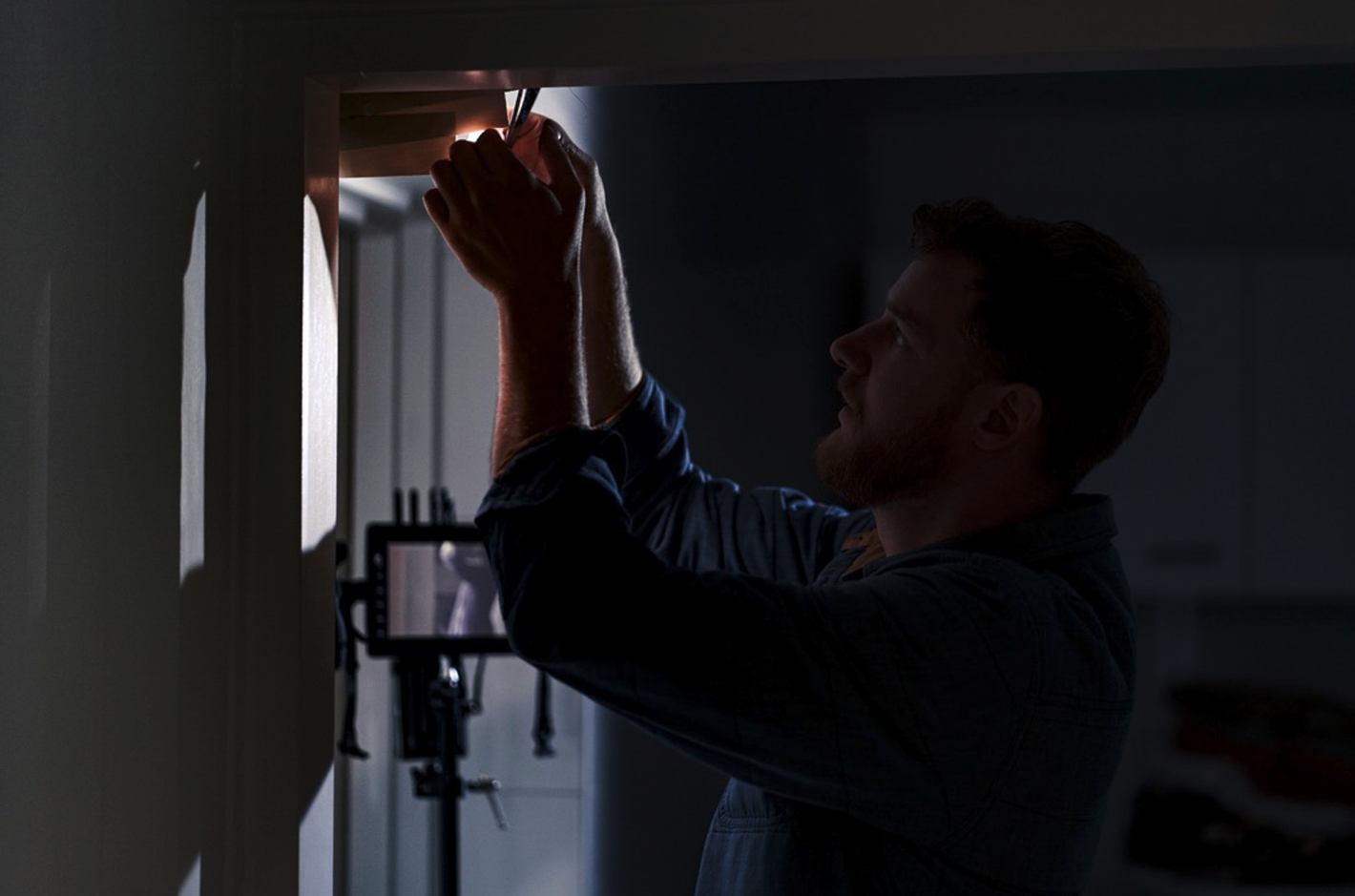 Man die een raam of kast ophangt of repareert, met een camera of monitor in de achtergrond.