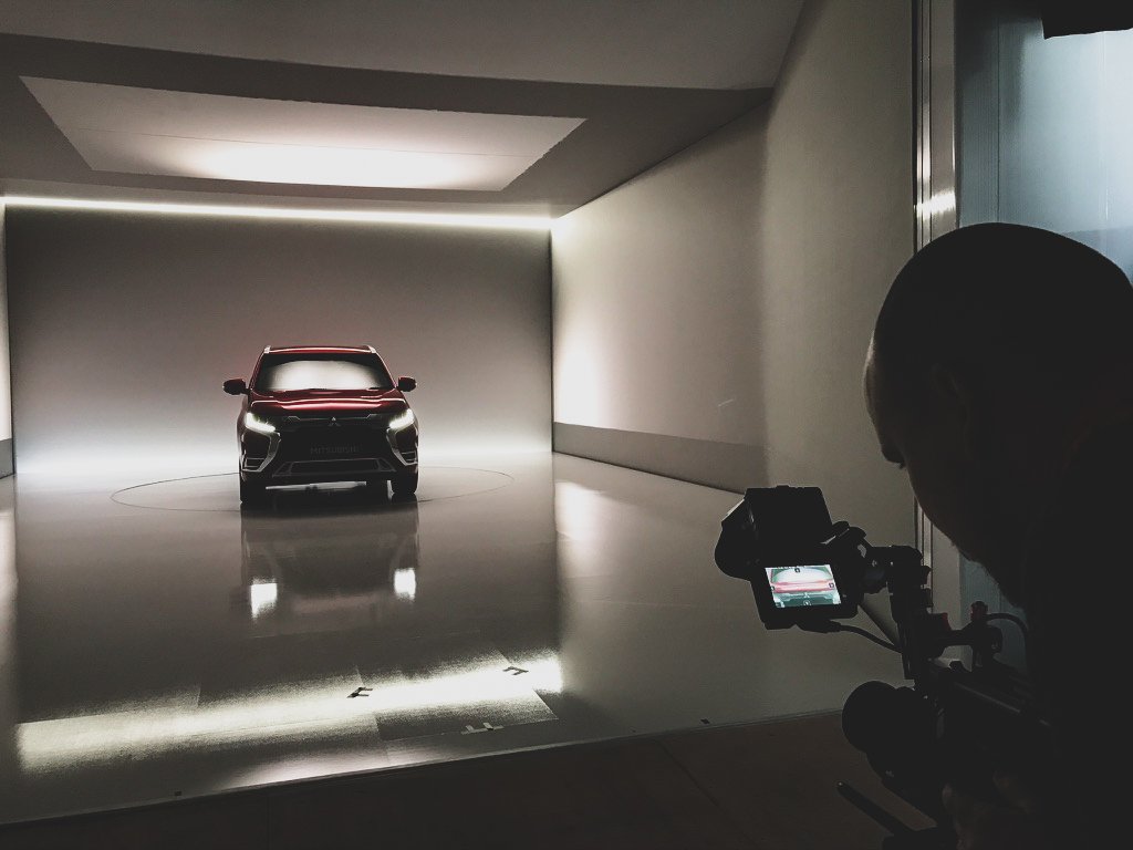 A red car is being photographed in a white studio with minimal lighting.