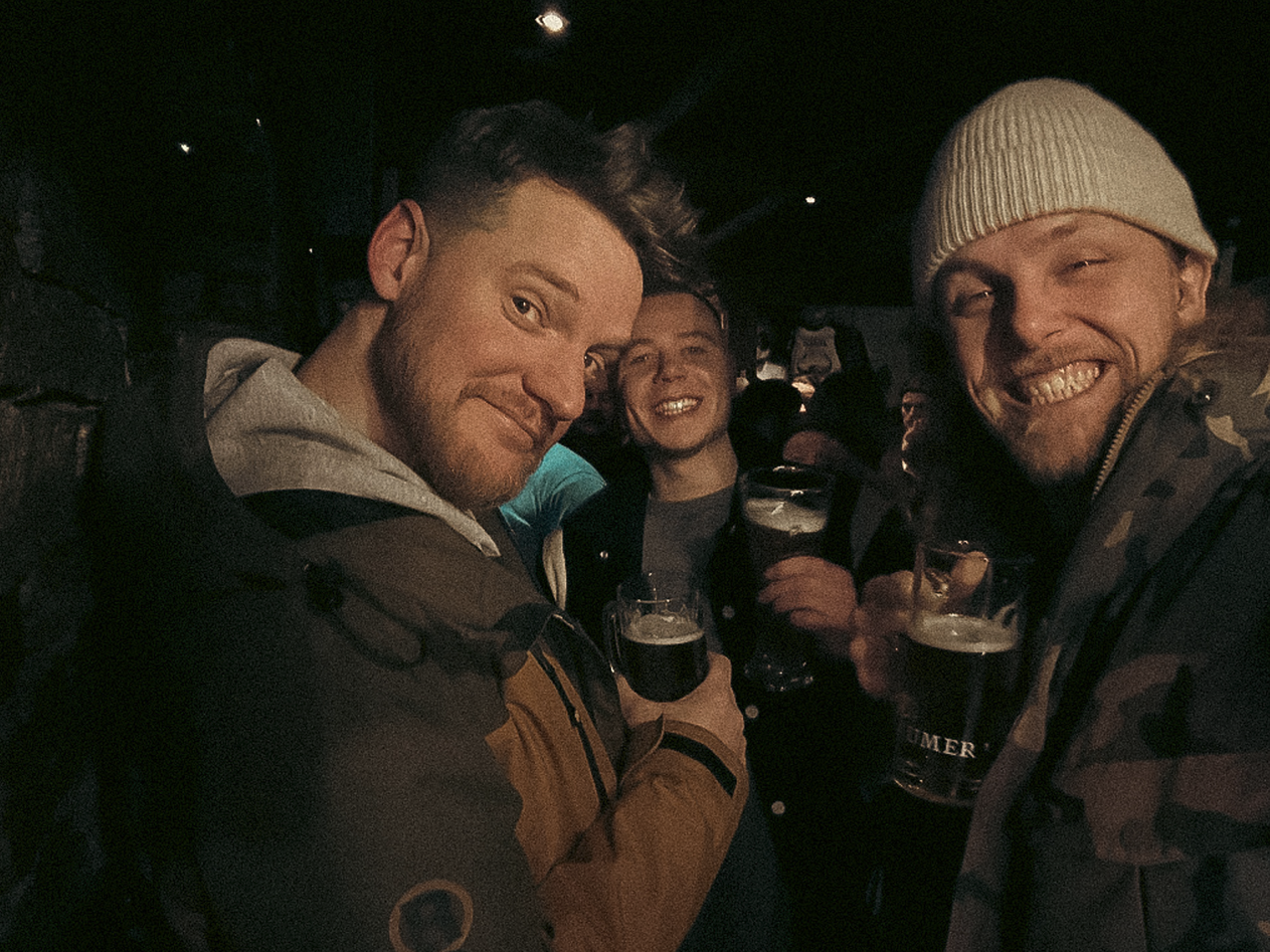 Vijf personen die samen lachen en drinken in een bar, in een gezellige sfeer, 's avonds.