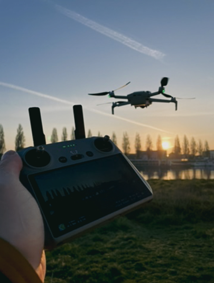 A person flying a drone with a remote control near a body of water during sunset