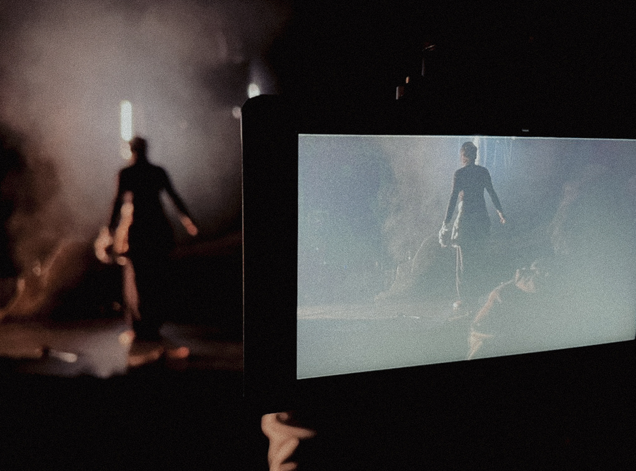 Een persoon filmt een scène met een smartphone waarop een vrouw in een donkere jurk te zien is, staande in een mistige omgeving.