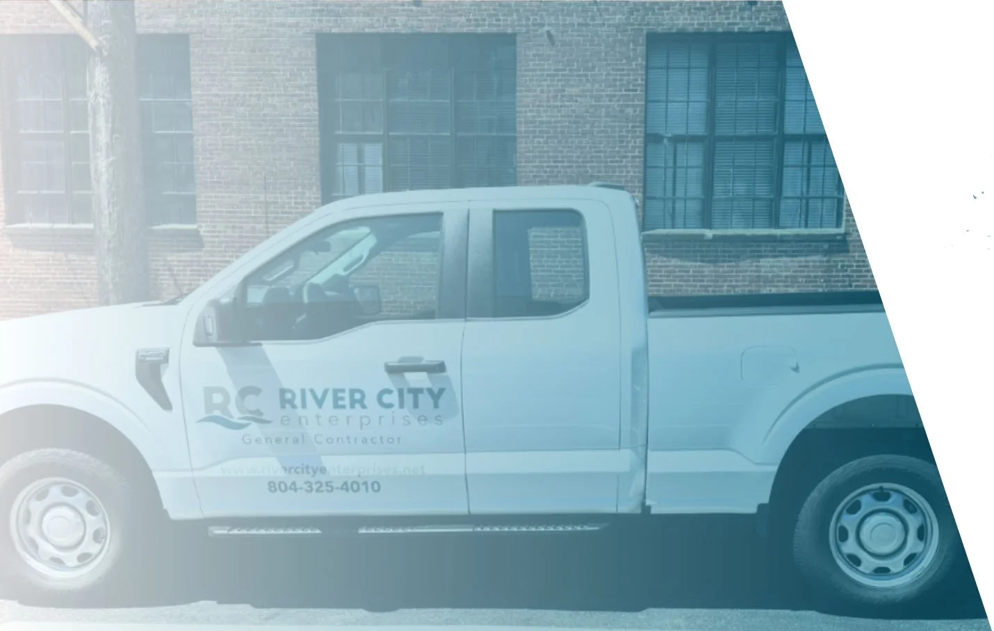 White pickup truck with 'River City Enterprises' logo parked in front of a brick building with barred windows.