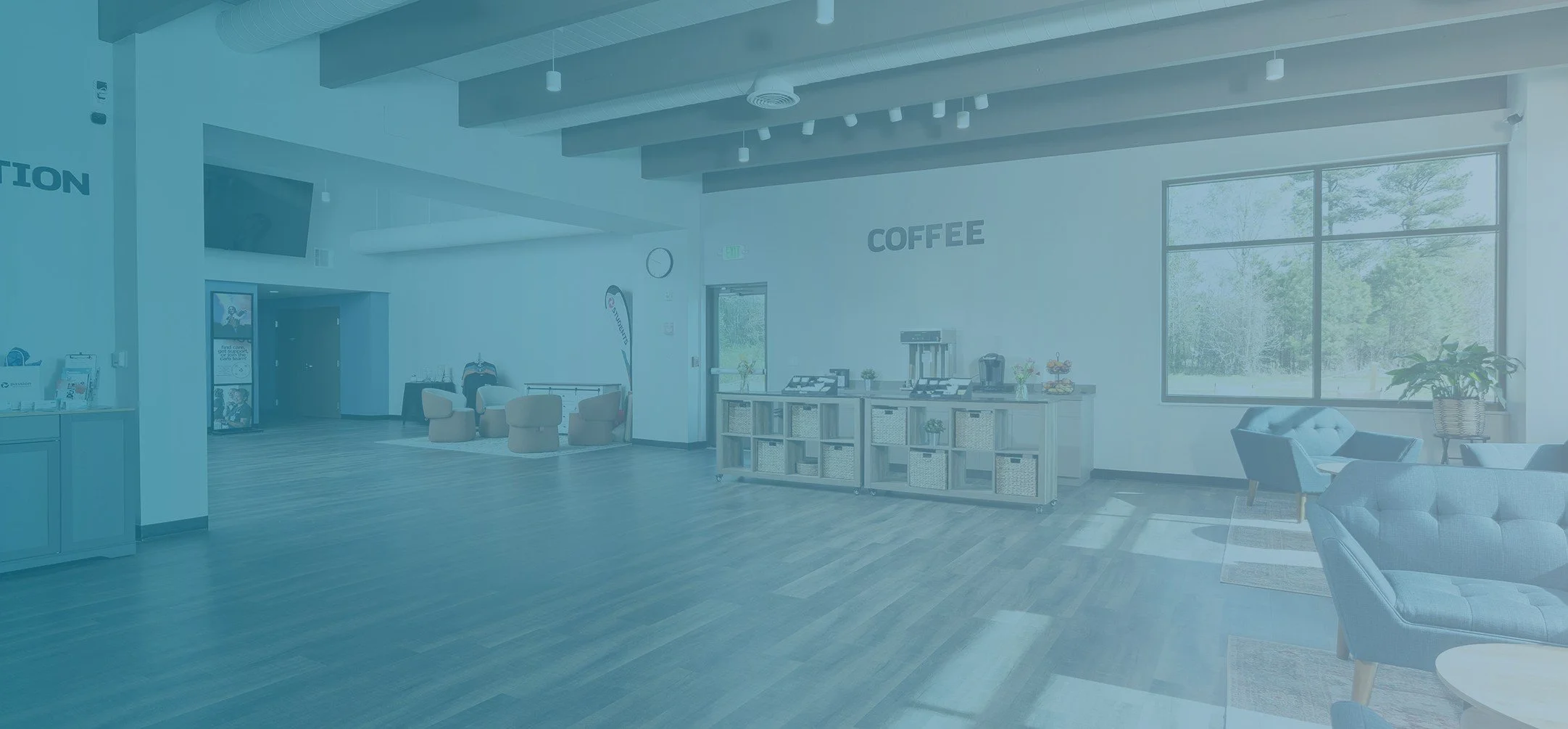A spacious modern lounge or cafe area with large windows, seating, coffee station, and decorative plants.