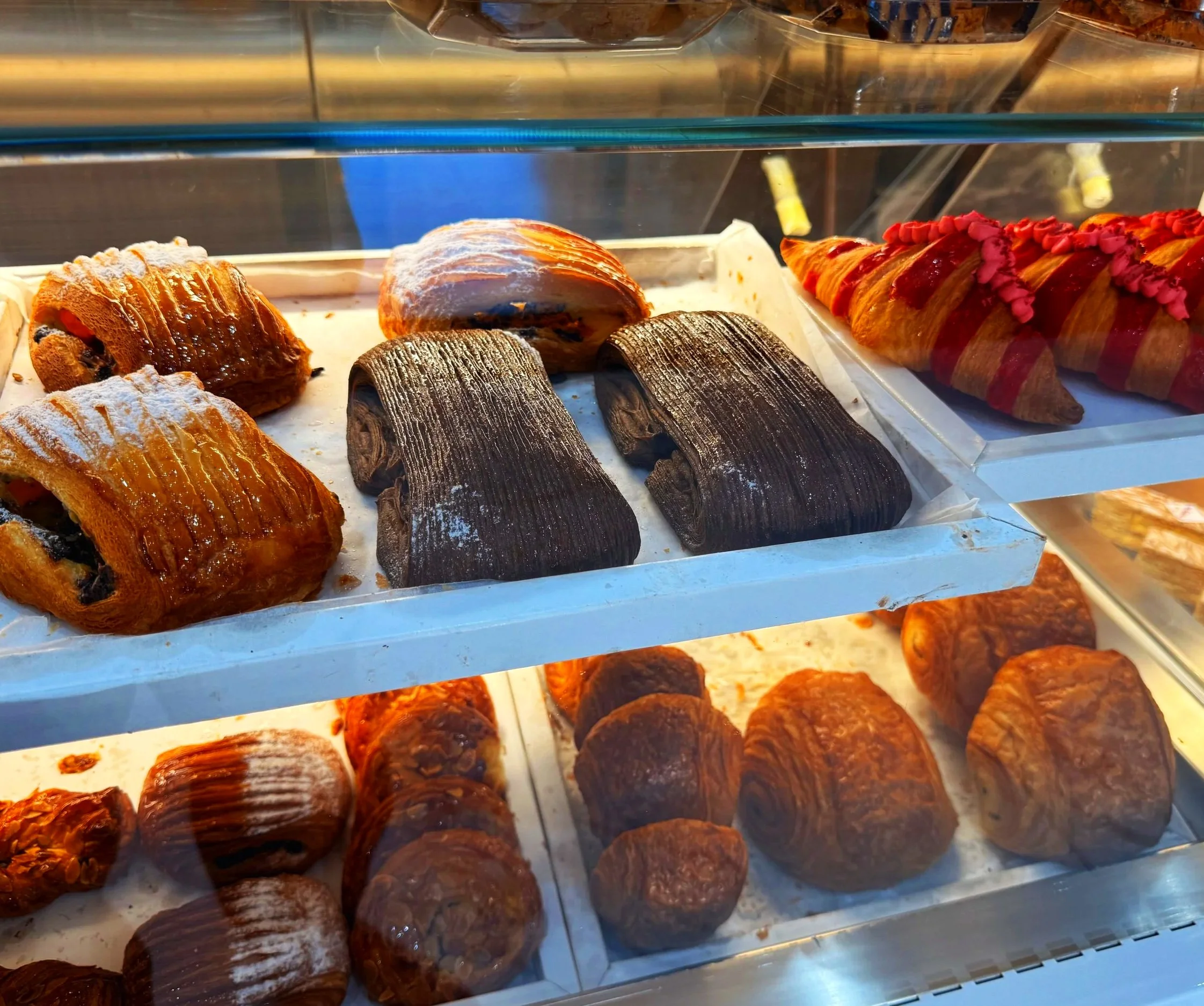 Vitrine de pâtisseries françaises, incluant des éclairs au chocolat, des croissants décorés avec du glaçage rose, et d'autres viennoiseries.