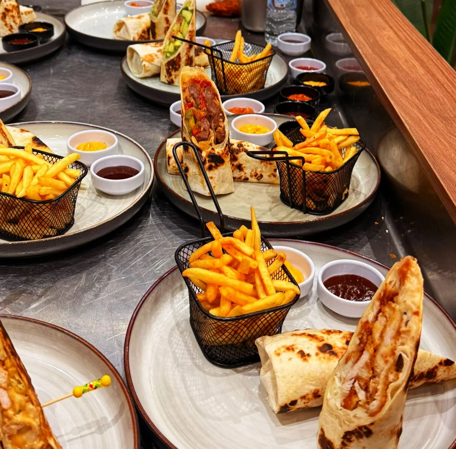 Assiette avec un wrap coupé en deux, frites, et plusieurs petites sauces.