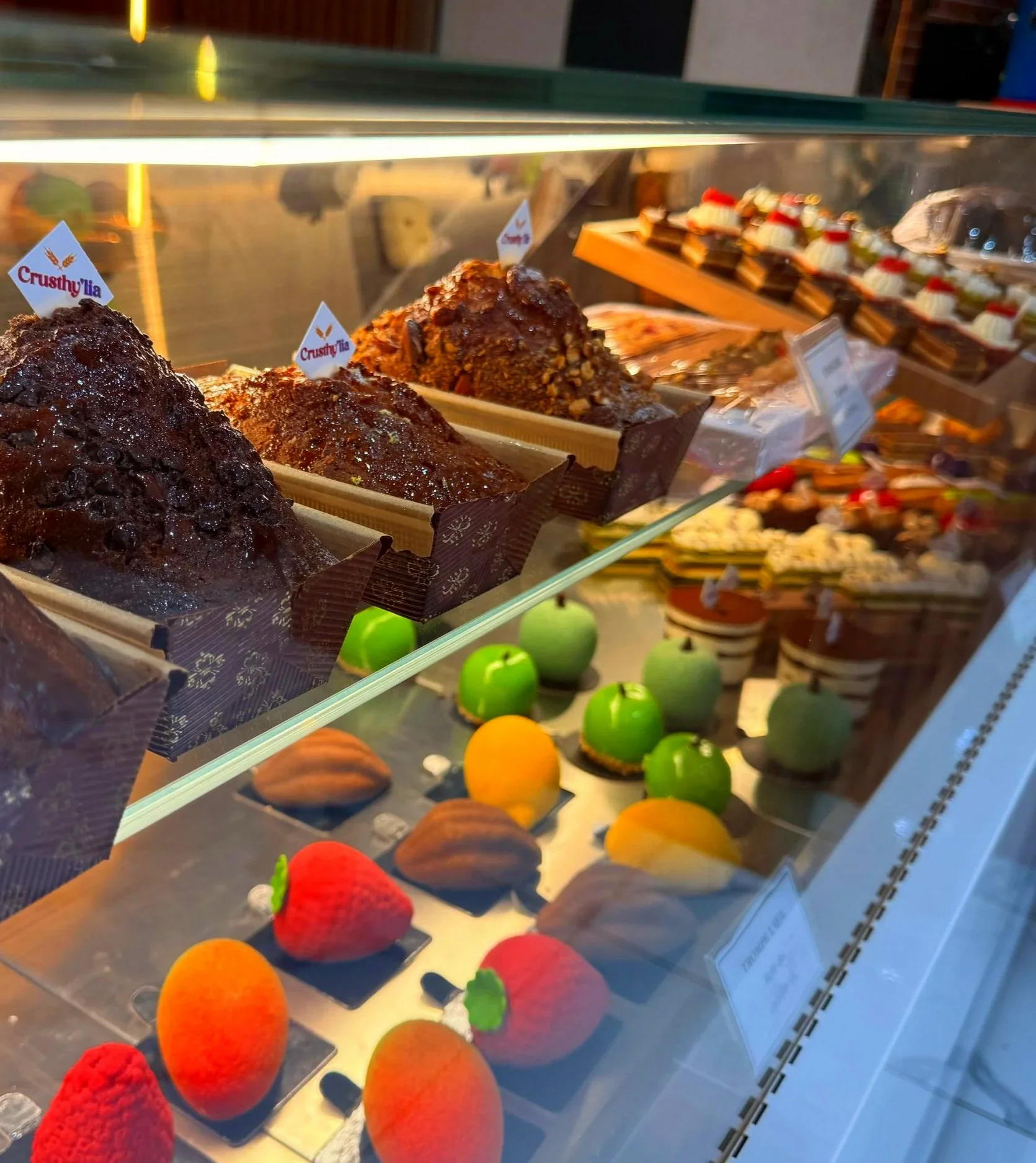Vitrine affichant différentes pâtisseries, notamment des gâteaux en forme de fruits et des éclairs au chocolat.