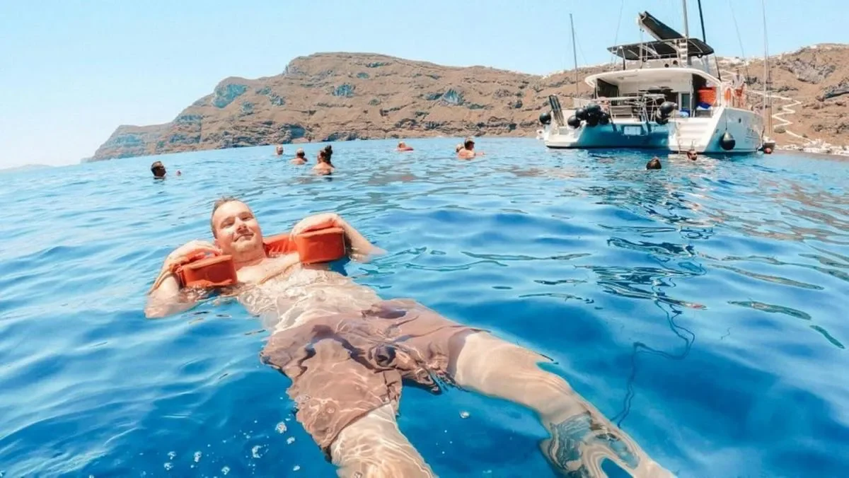 People swimming at the sea near a catamaran.