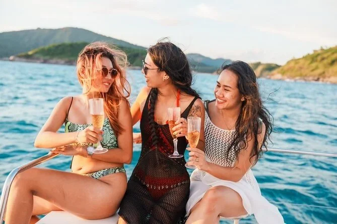Three women sitting on a boat, holding glasses of champagne, enjoying a sunny day on the water.