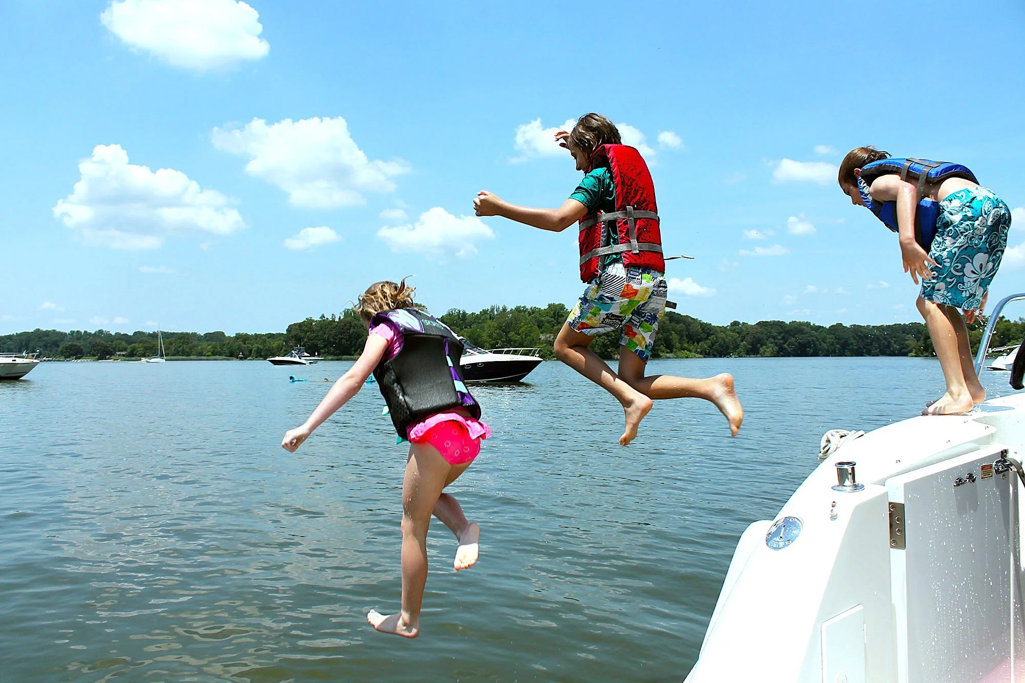 Three children jumping off a boat into the sea on a sunny day.