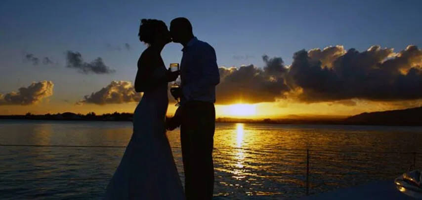 Silhouetted couple on catamaran at sunset.