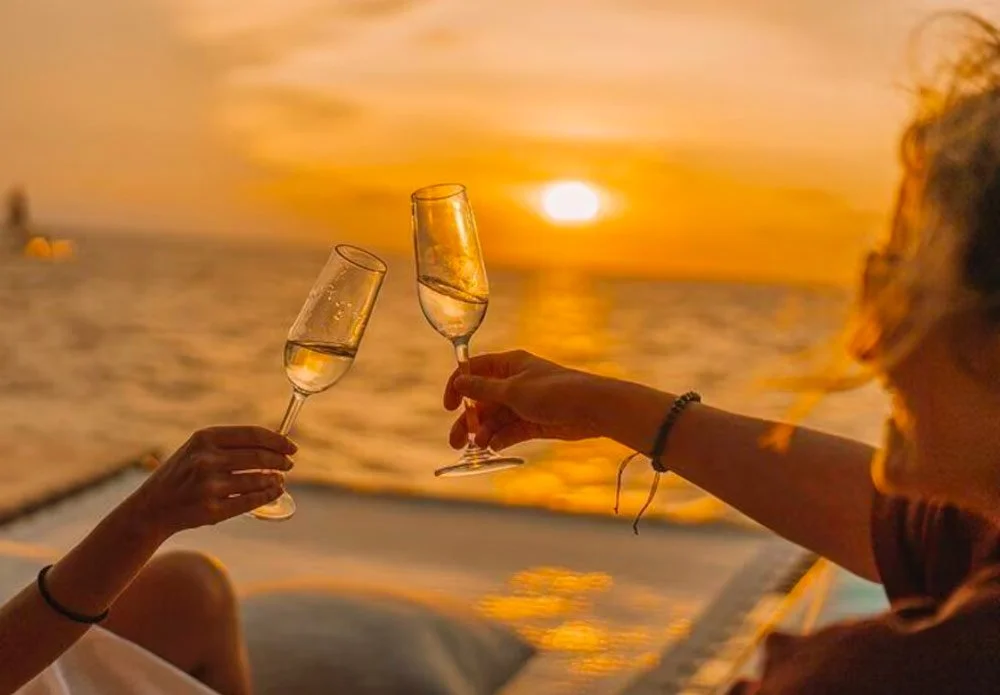 Two women clinking glasses of champagne during a sunset on a boat.