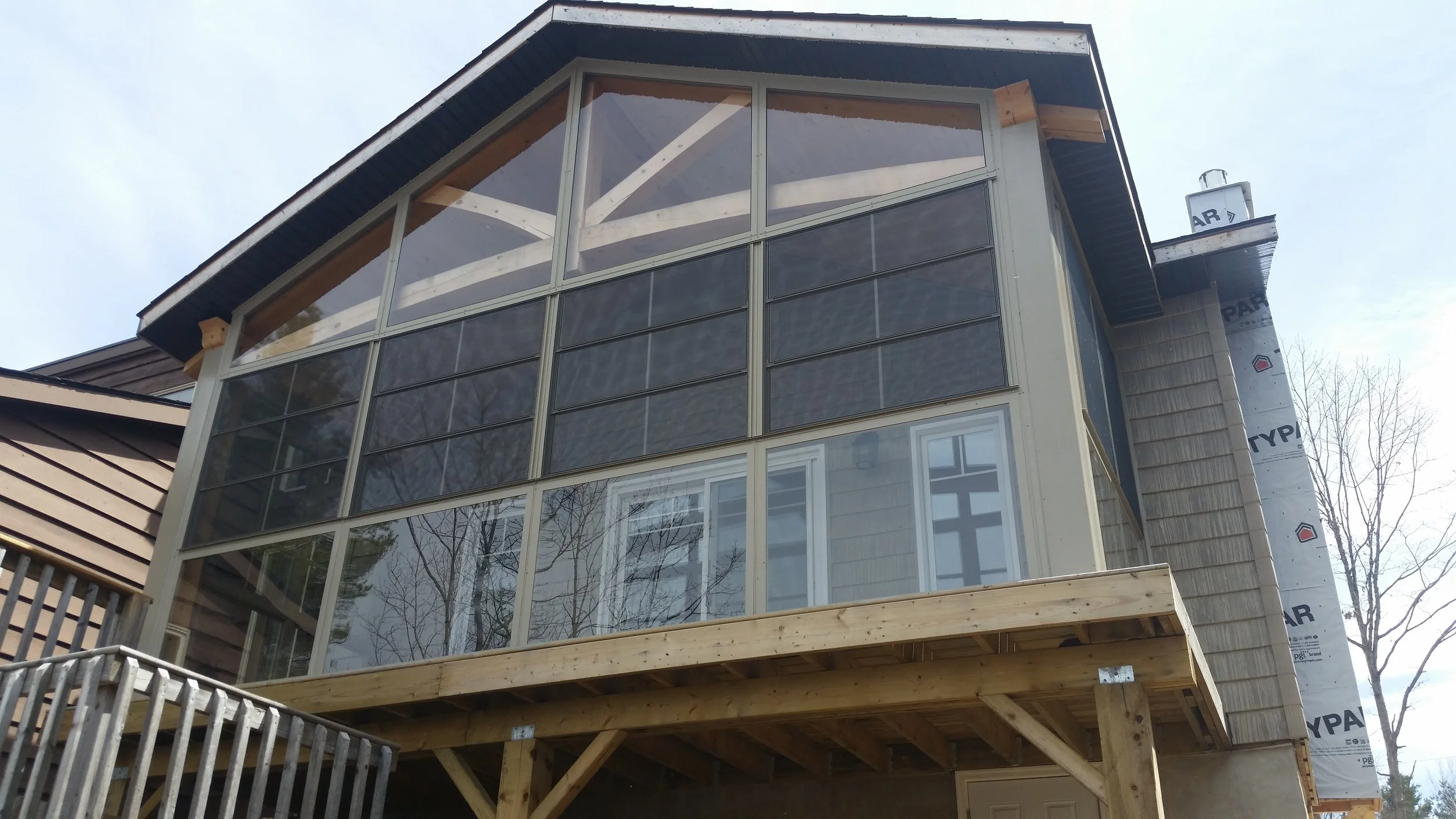 A multi-story house under construction with large glass windows and a wooden balcony.