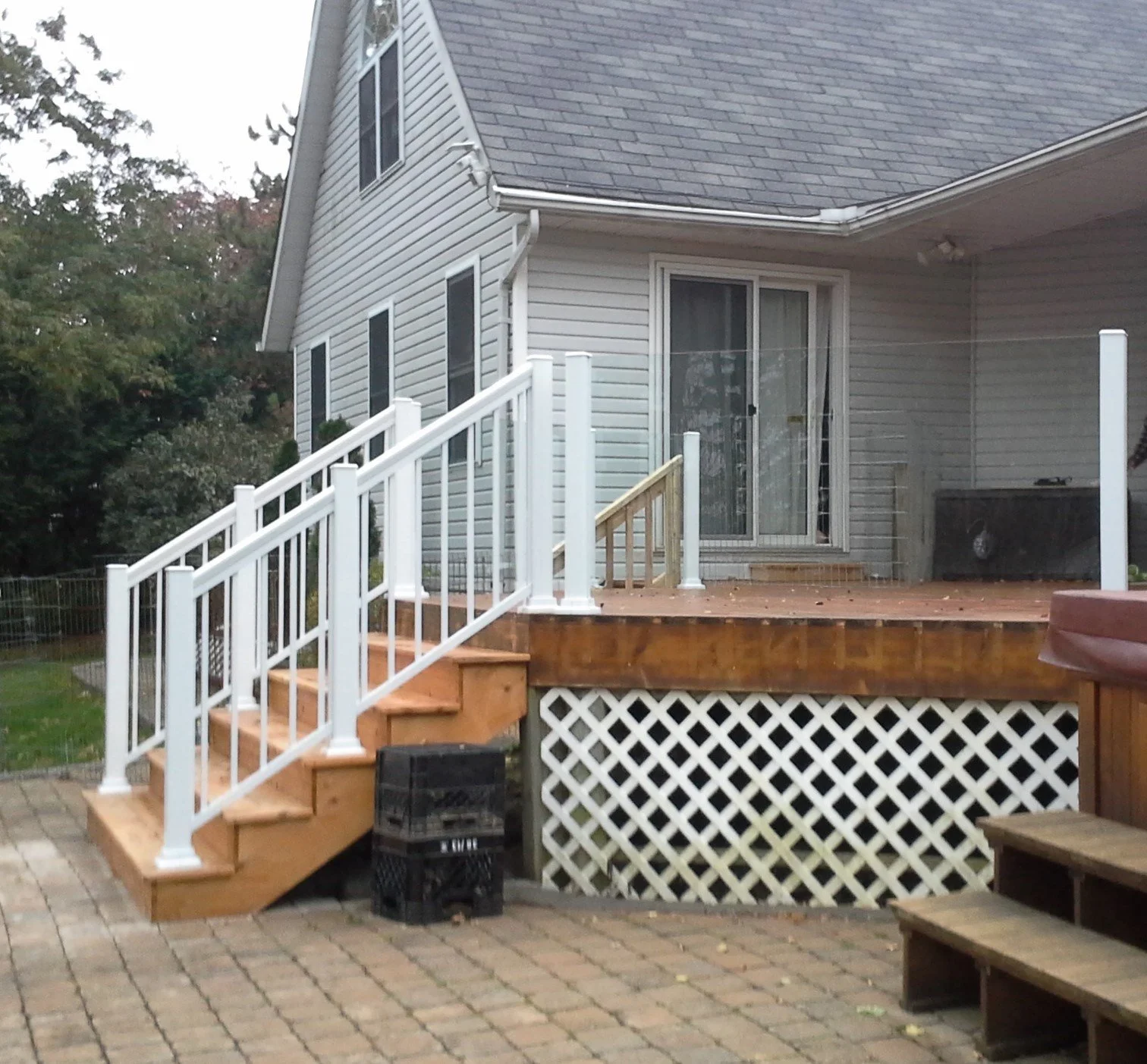 New wooden deck with white railings and stairs attached to a house with sliding glass door, surrounded by backyard with trees.