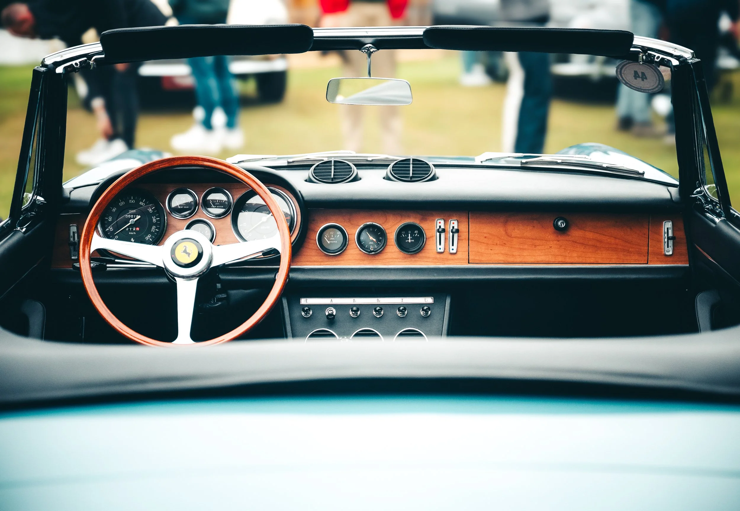 Interieur van een klassieke Ferrari met een houten dashboard, ronde meters en een houten stuurwiel, gezien vanaf de bestuurderskant.