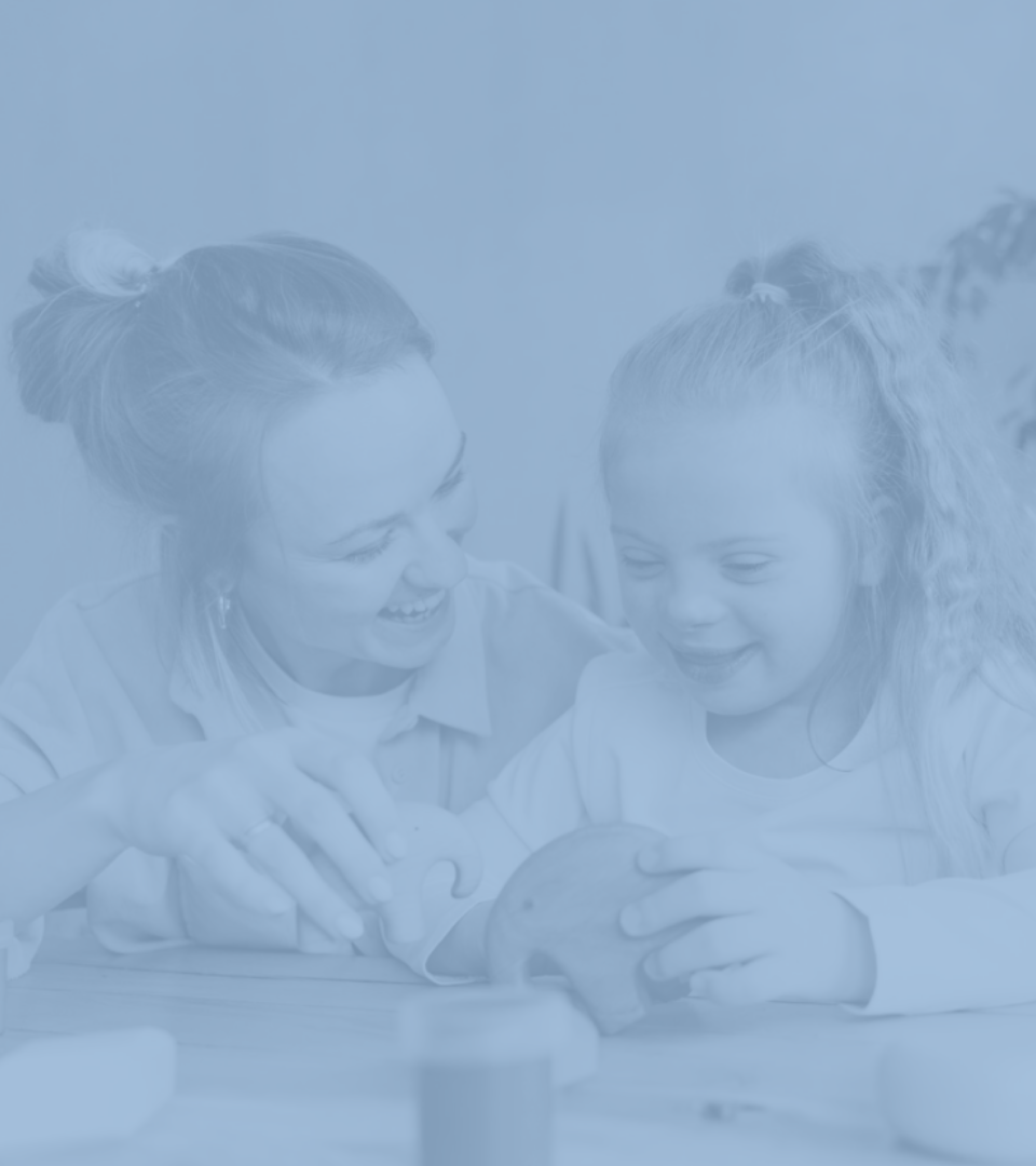 A woman and a little girl sitting at a table, smiling and engaging in a craft activity.