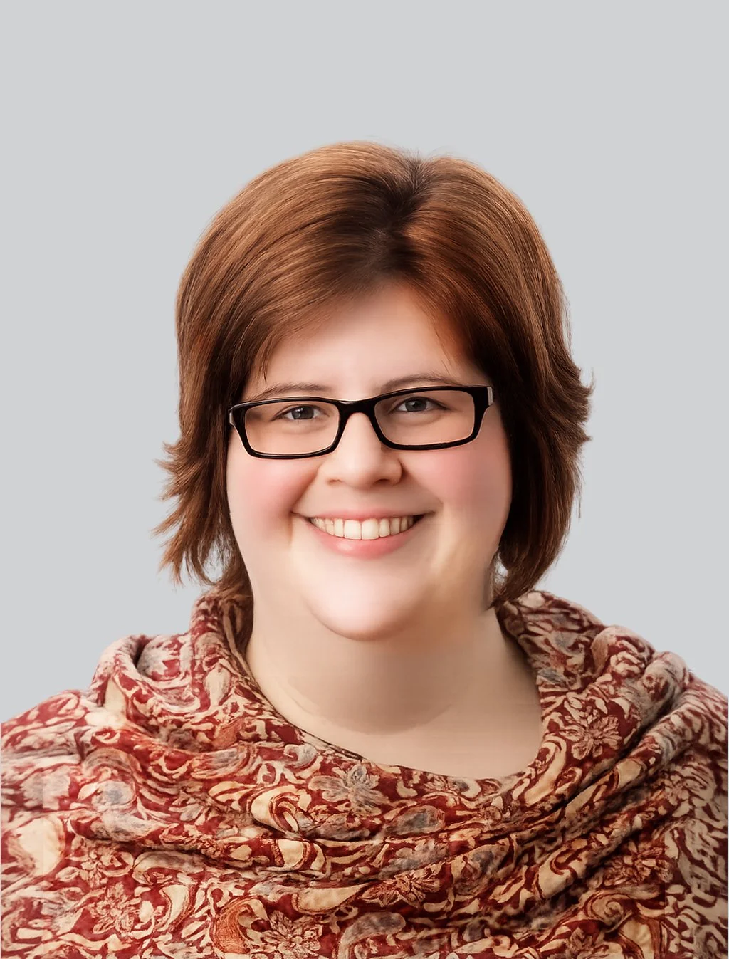 A woman with short brown hair, glasses, and a patterned shawl smiling against a light gray background.