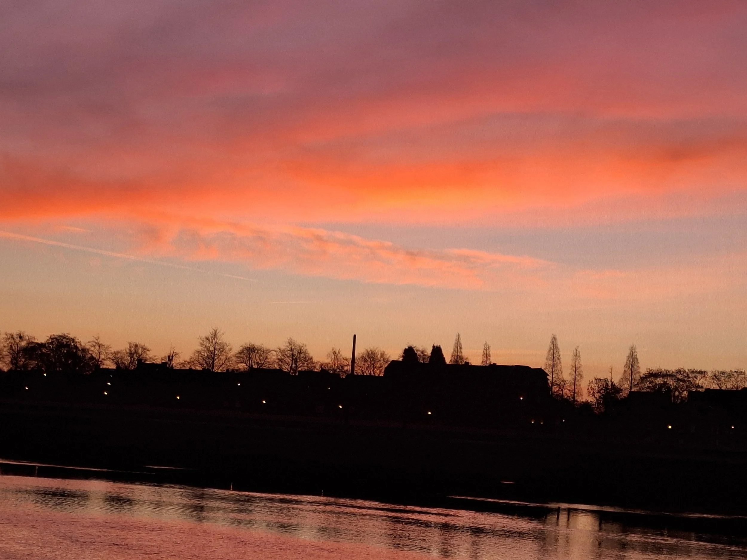 A sunset over a river with a bridge in the foreground and silhouetted trees on the horizon.