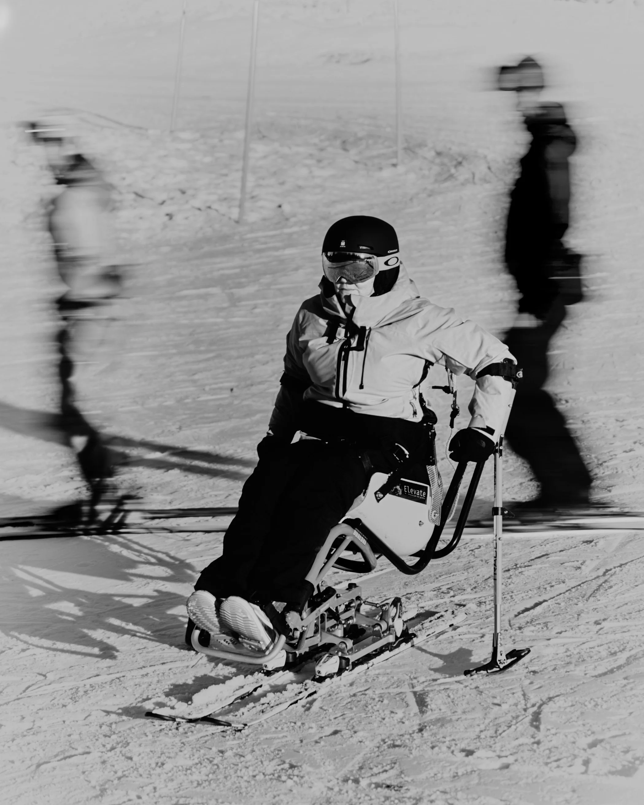 An adaptive skier on a snowy slope, with blurred skiers in the background.
