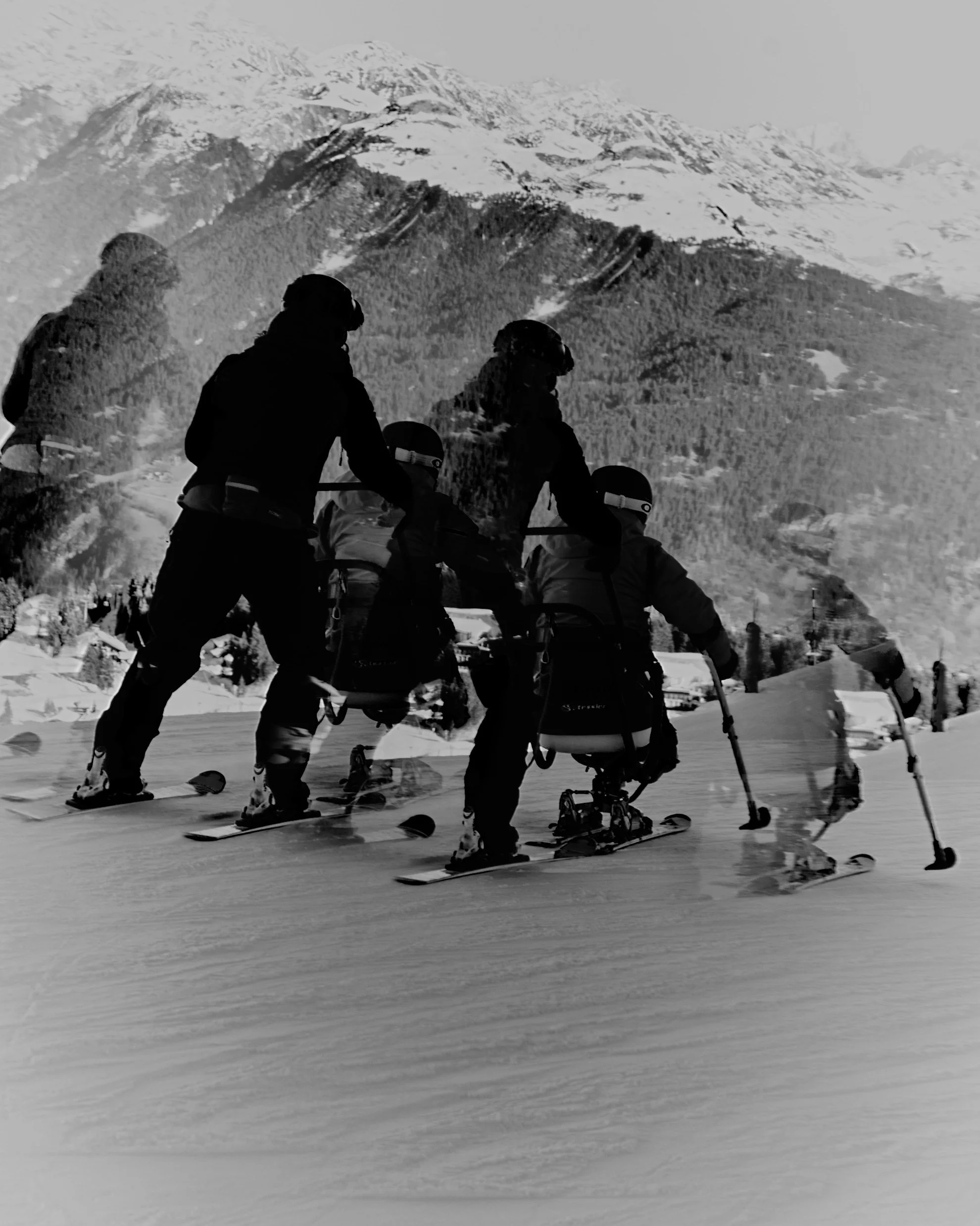 A motion blur image of adaptive ski-ing on a snow-covered mountain with a backdrop of snow-capped peaks.