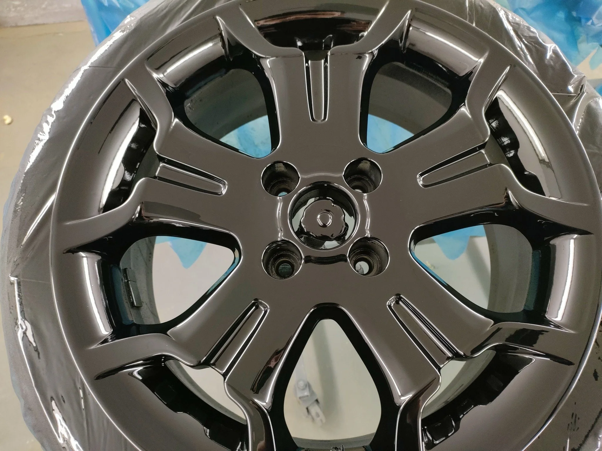 A shiny, metallic vehicle alloy wheel rim with a modern design, resting on a surface covered with protective wrapping.