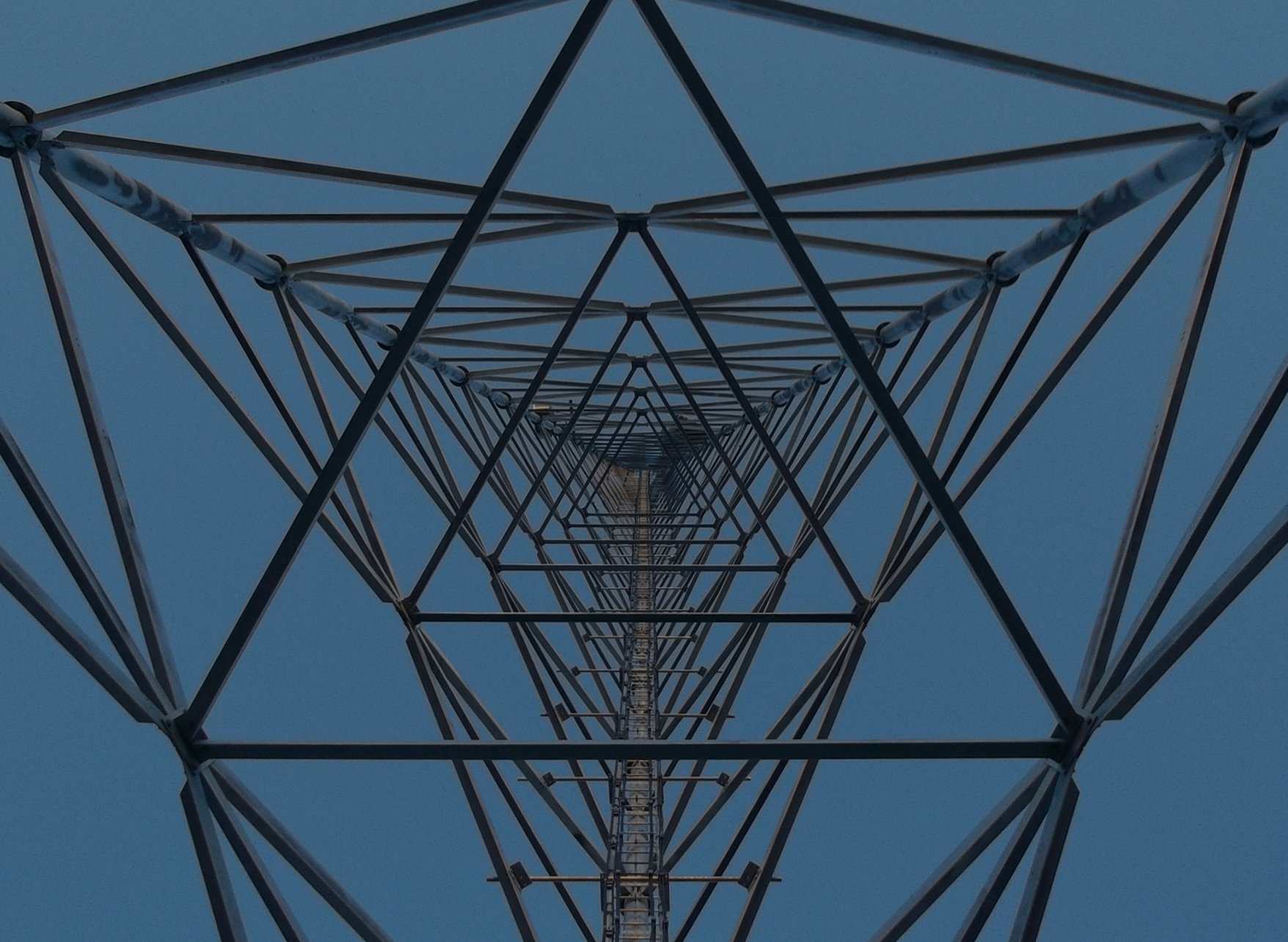 Looking up at a tall metal tower structure against a clear blue sky, showing the intricate framework and design of the tower.