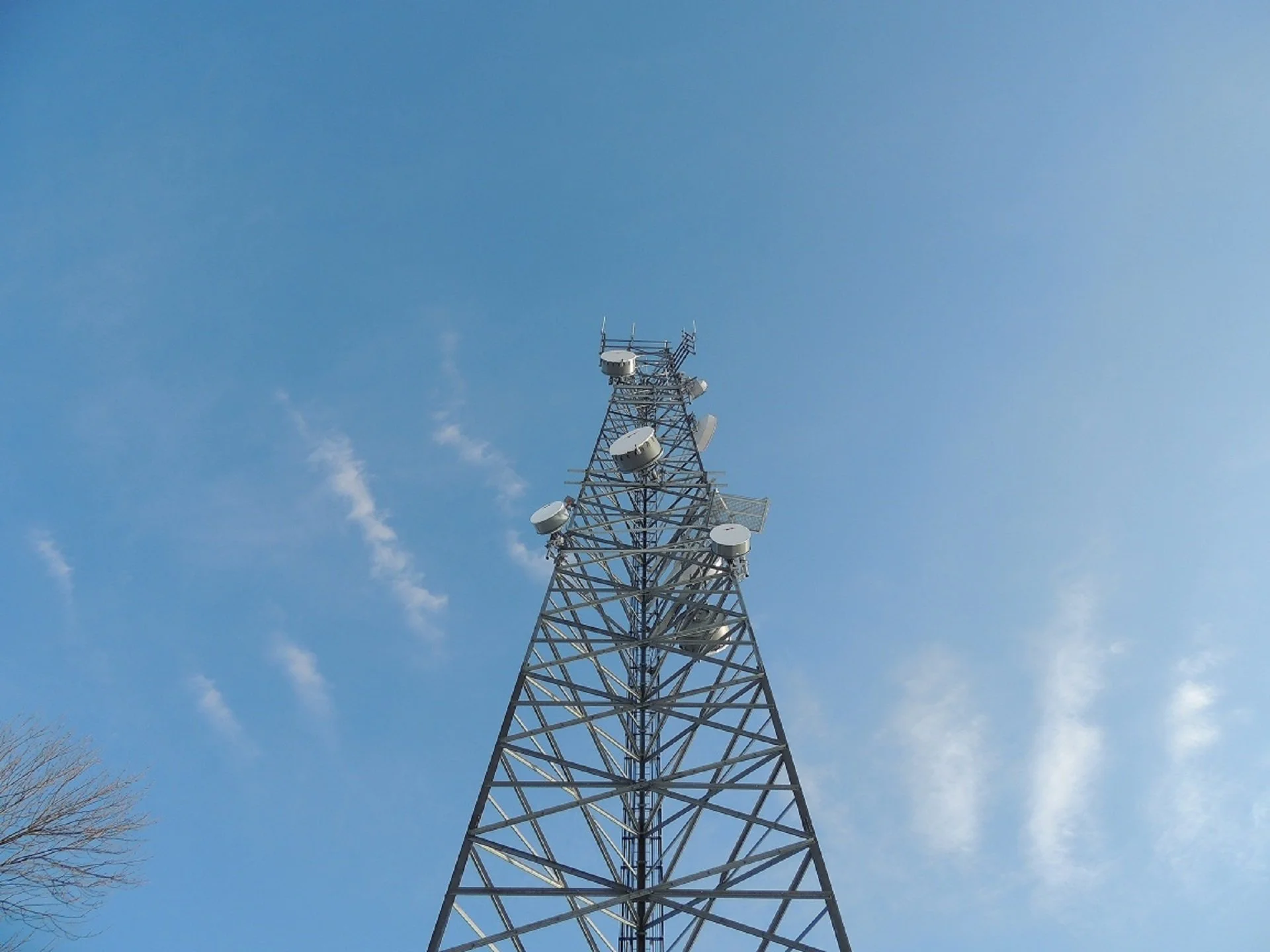 A tall communication tower with multiple antennas and dishes against a blue sky with wispy clouds.