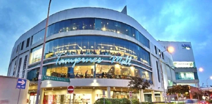 Modern, multi-story shopping mall with large glass windows and signage that reads "Tamjames Mall" at sunset.