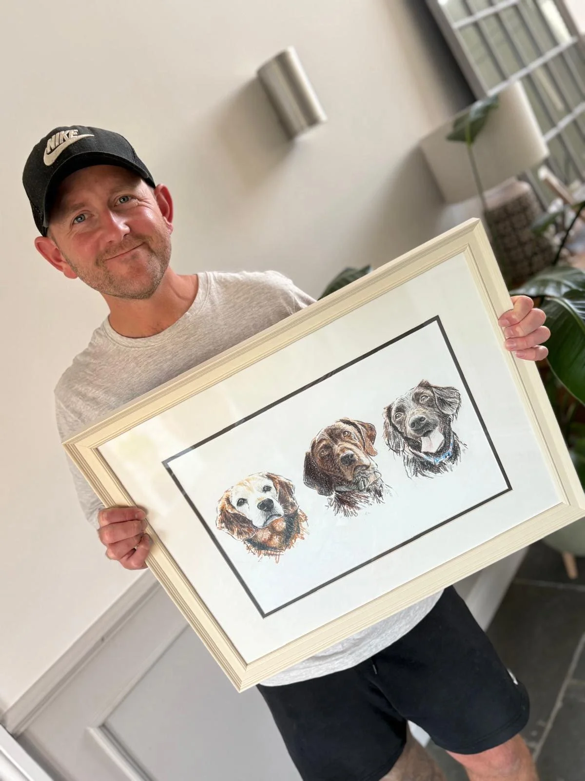 Customer holding framed hand drawn pet portrait of three dogs