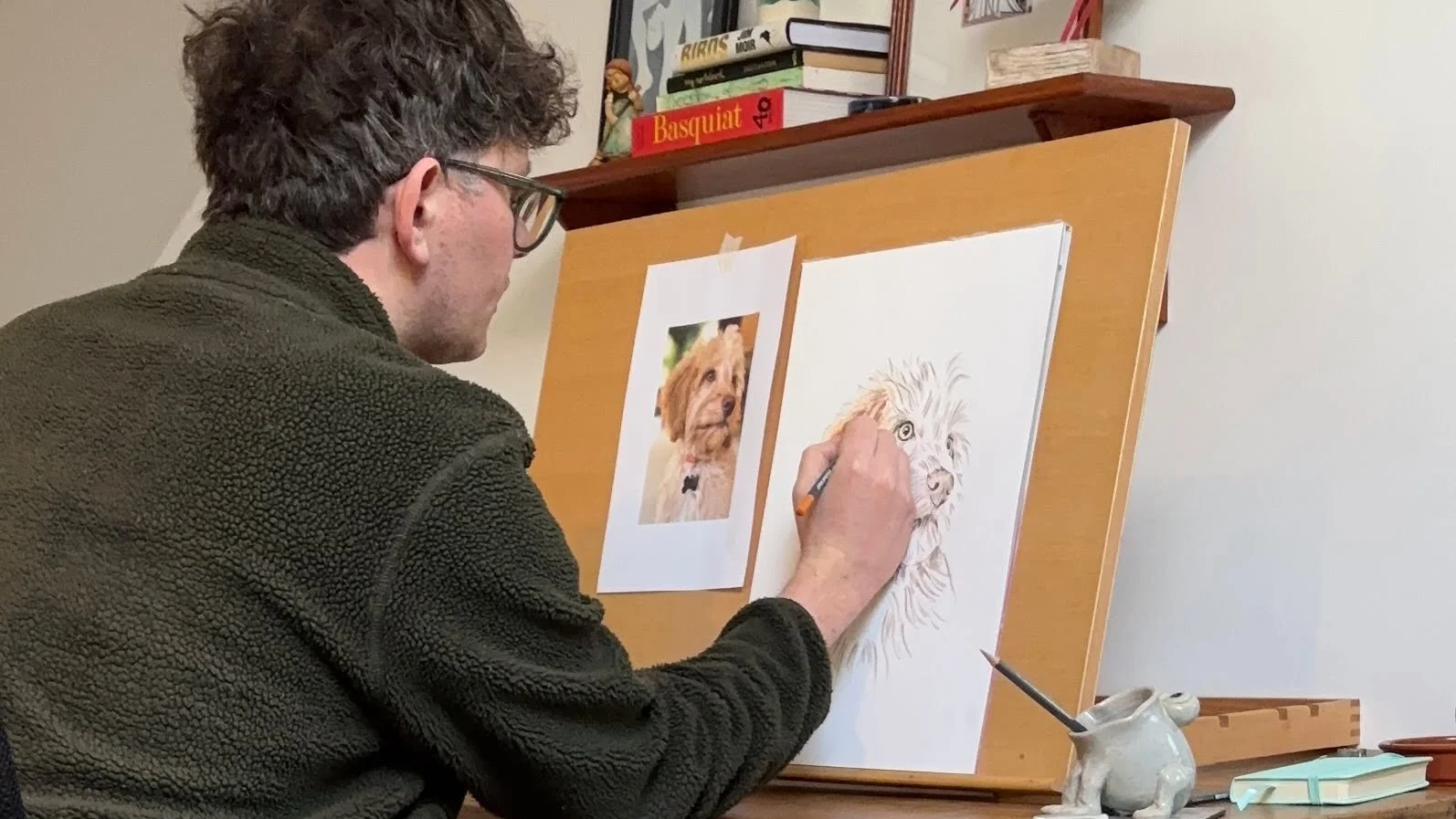 Artist Jonny Atkinson drawing a pet portrait in coloured pencil at a desk, commission in progress