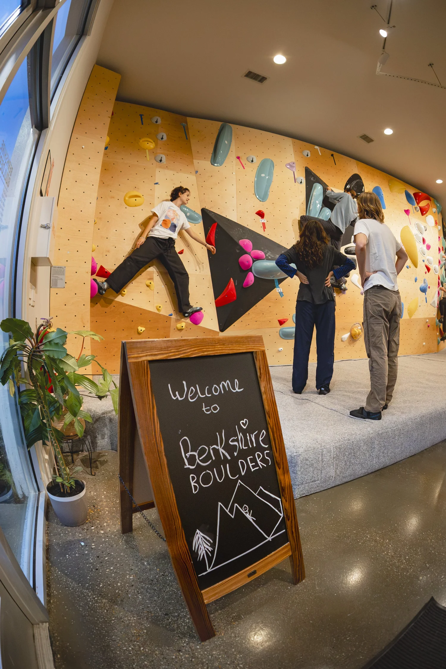 Welcome to Berkshire Boulders chalkboard sign in front of climbers on the wall