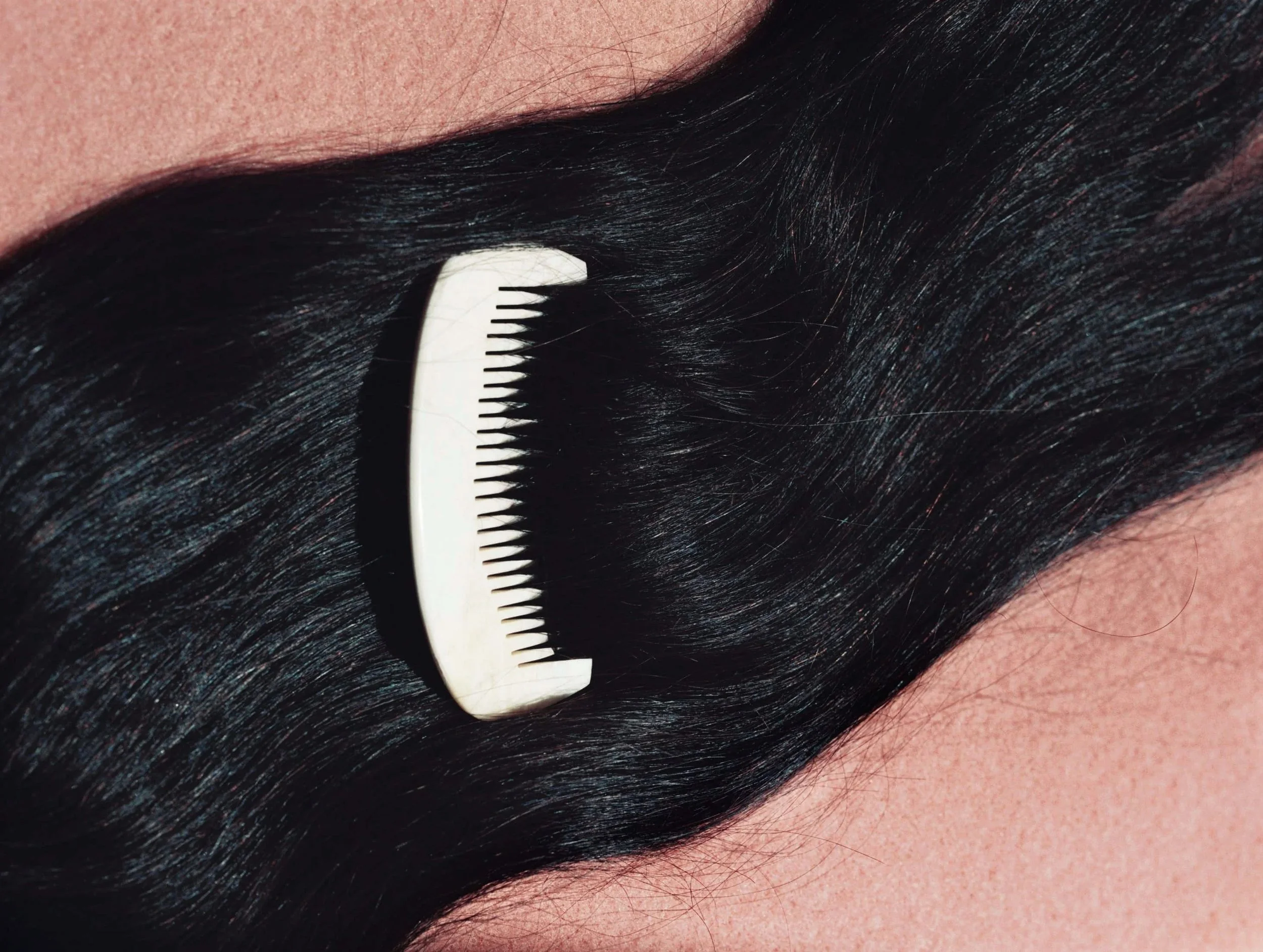 Close-up view of wavy black hair with a white comb running through it.