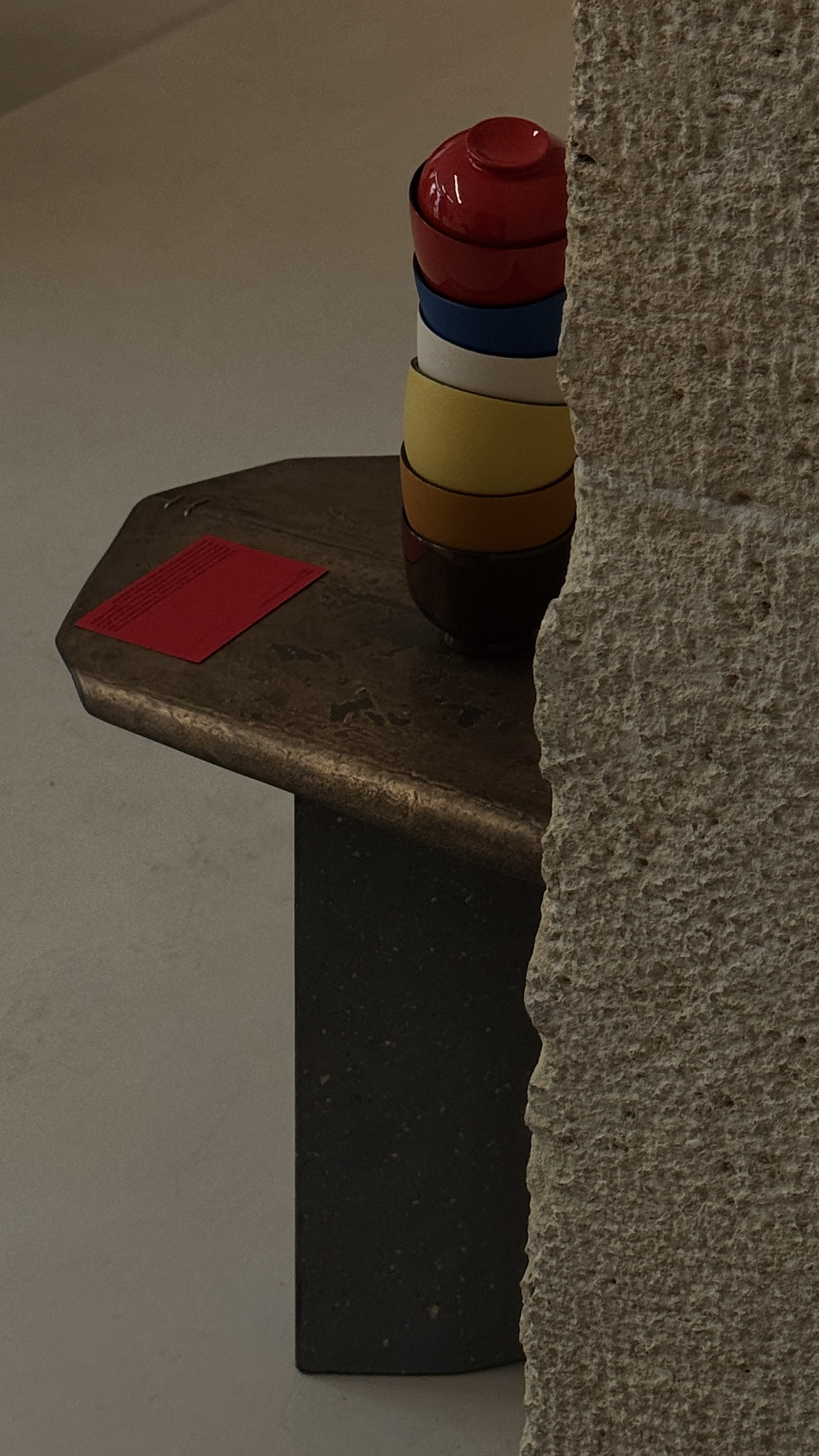 Stack of colorful plastic bowls placed on a small dark table next to a rough-textured stone wall.