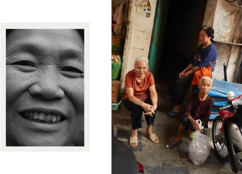 Three elderly women sitting and standing outside a building, with one holding a plastic bag, and a motorcycle nearby.