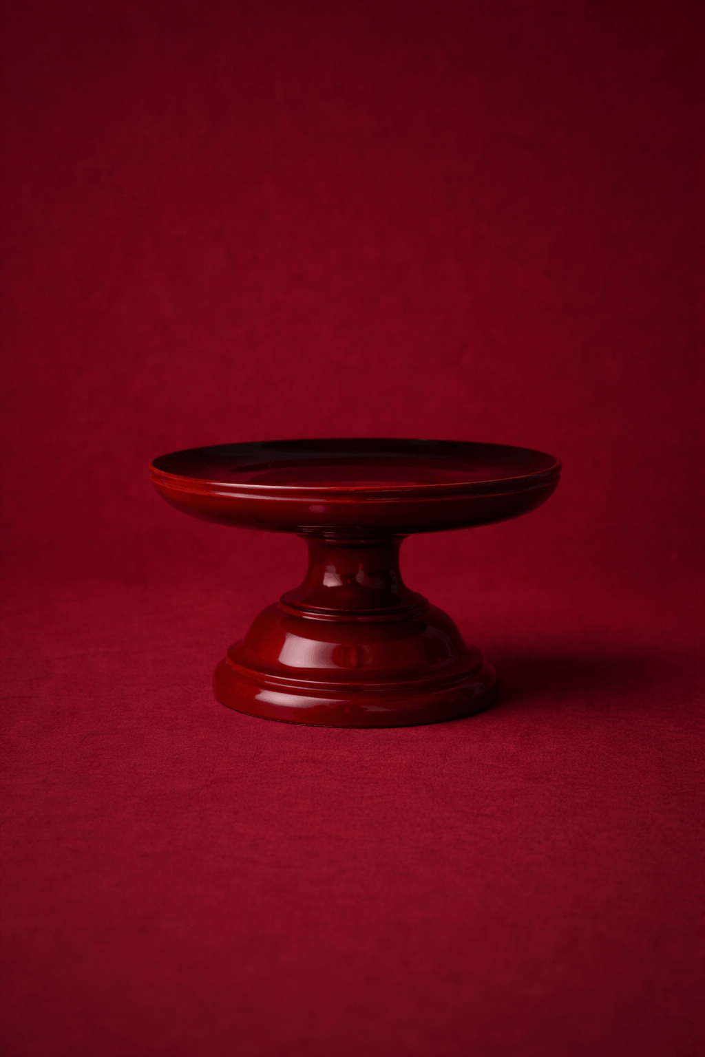 A dark red, reflective pedestal stand against a matching red background.