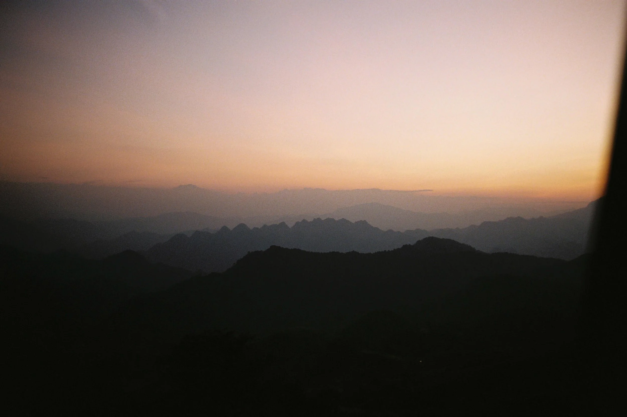 A mountain landscape during sunset with a gradient sky from pink to purple and silhouettes of mountain ridges.
