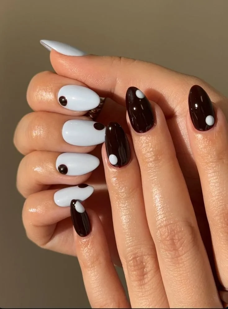Close-up of manicured fingernails with black and white nail polish and decorative dots.