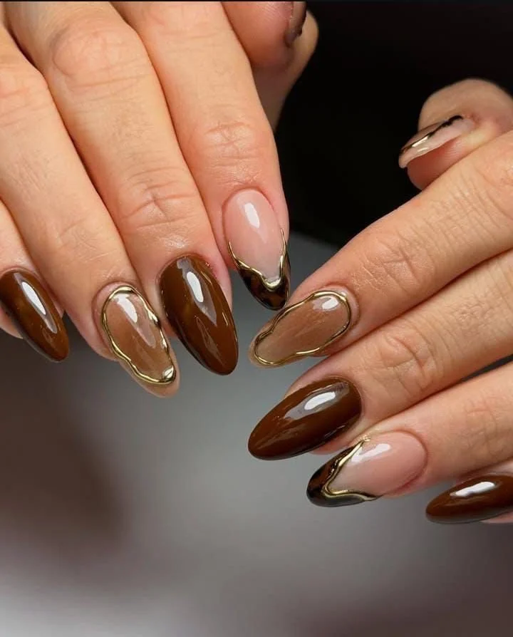 Close-up of a person's hands with manicured nails featuring a brown and nude color palette and gold accents on the nails.