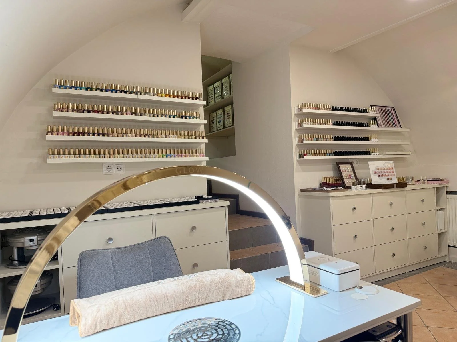 Display of multiple nail polish bottles on white shelves in a nail salon or spa.