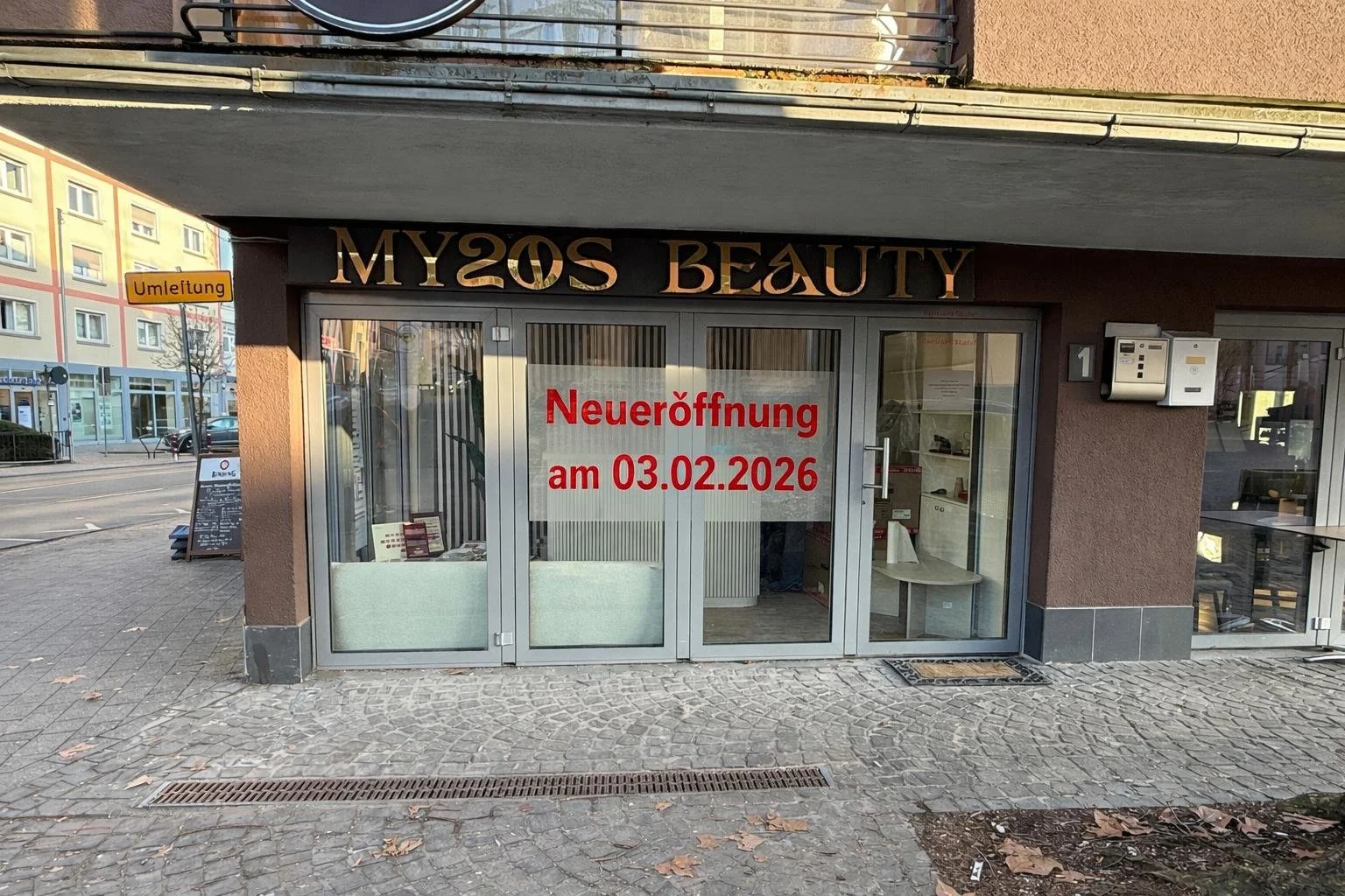  storefront for MY2OS BEAUTY with a sign in the window announcing grand opening on February 3, 2026, in German. The store has glass doors and windows, and there's a sign on the sidewalk outside.