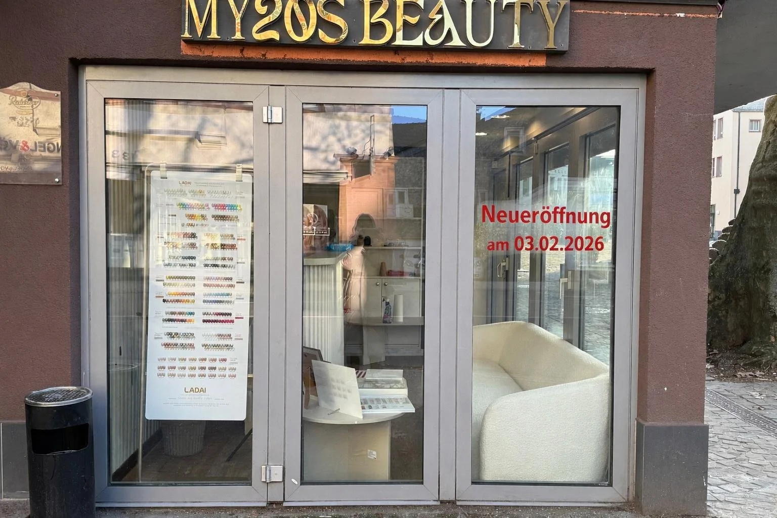 The storefront of MY 20'S BEAUTY with glass doors displaying a sign in red indicating it will reopen on February 3, 2026, and an interior with a white sofa and a table with brochures inside.